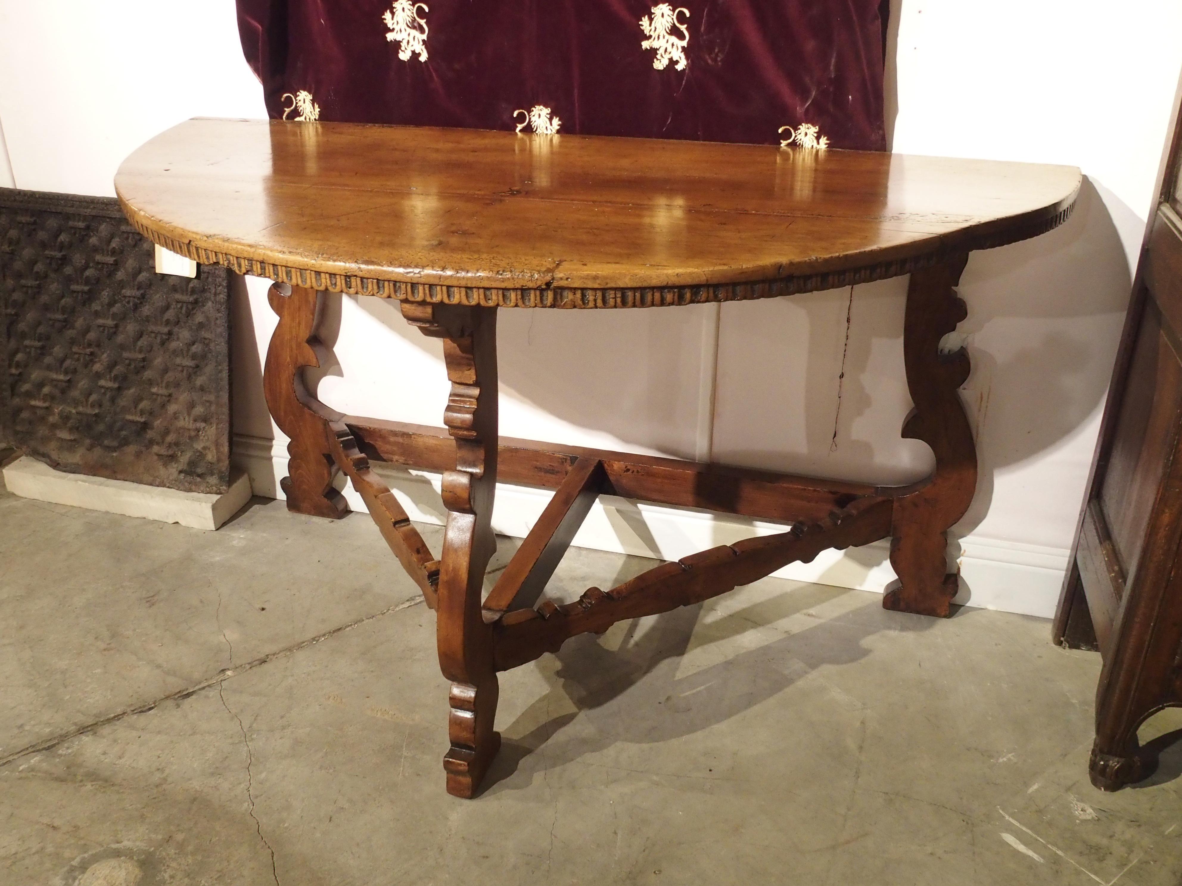 This half round table was made in Italy, in the early 1700s. Tables of this type were first constructed in the mid to late 1600s, heavily influenced by Spanish style. The linear scoop motif under the top is typically Italian, while the shaped lyre