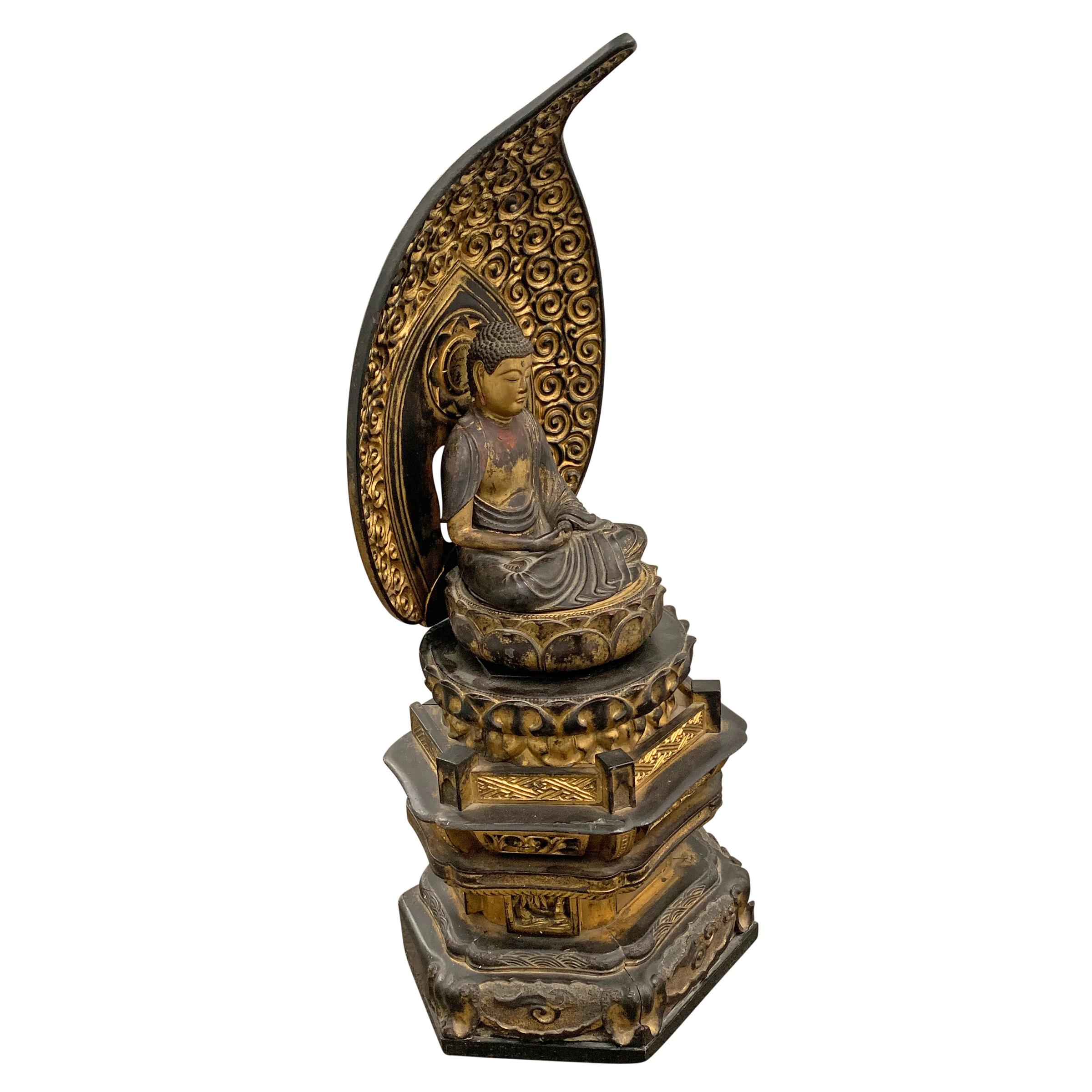 An incredible Edo Period Japanese gilt and lacquered carved wood shrine depicting a Bodhisattva with piercing glass eyes, a contemplative expression, and hands clasped in a meditation mudra, seated on a lotus throne under a wildly carved turbulent