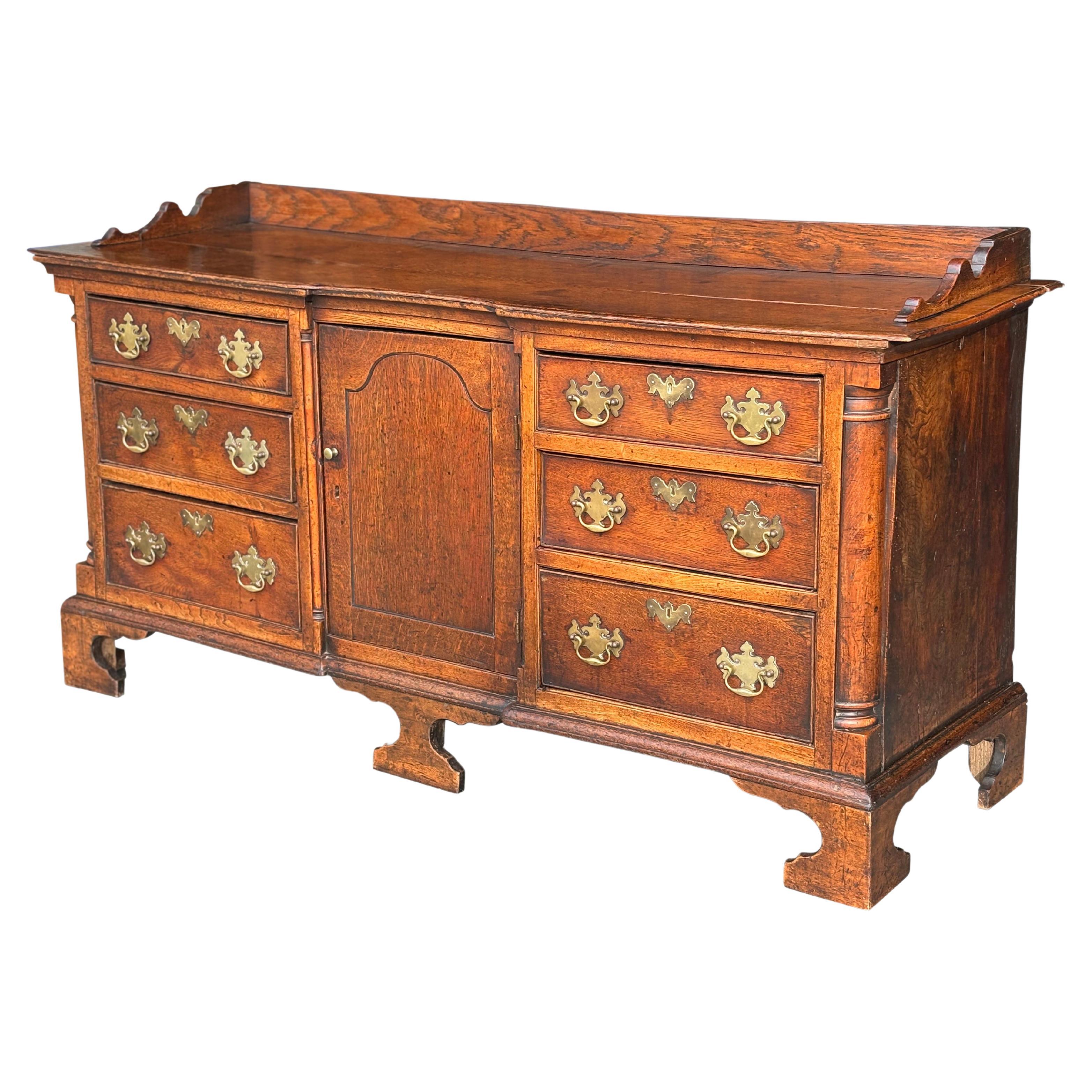 An 18th century Lancashire solid oak dresser base with fabulous colour and rich patina. Moulded rectangular planked top above a practical arrangement of a central cupboard flanked by 3 graduated drawers either side with brass plate handles and