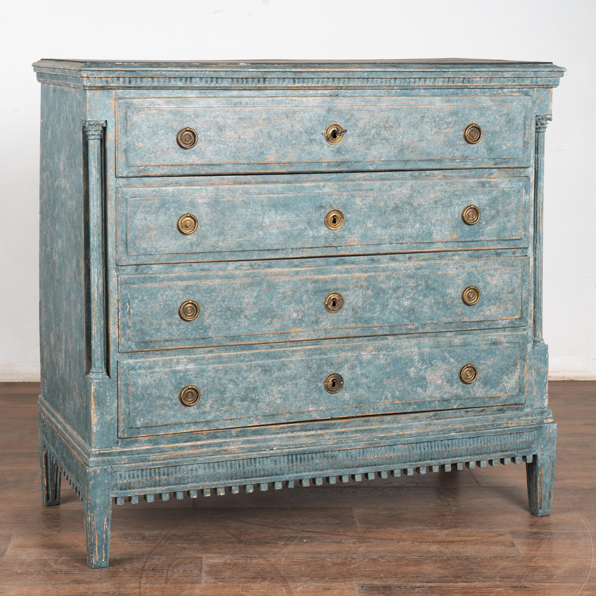 Grande commode en pin à quatre tiroirs flanquée de colonnes tournées et de sculptures décoratives sur le dessus et la jupe. 
La nouvelle finition peinte en couches bleues avec des nuances de blanc, appliquée par des professionnels, ajoute une touche
