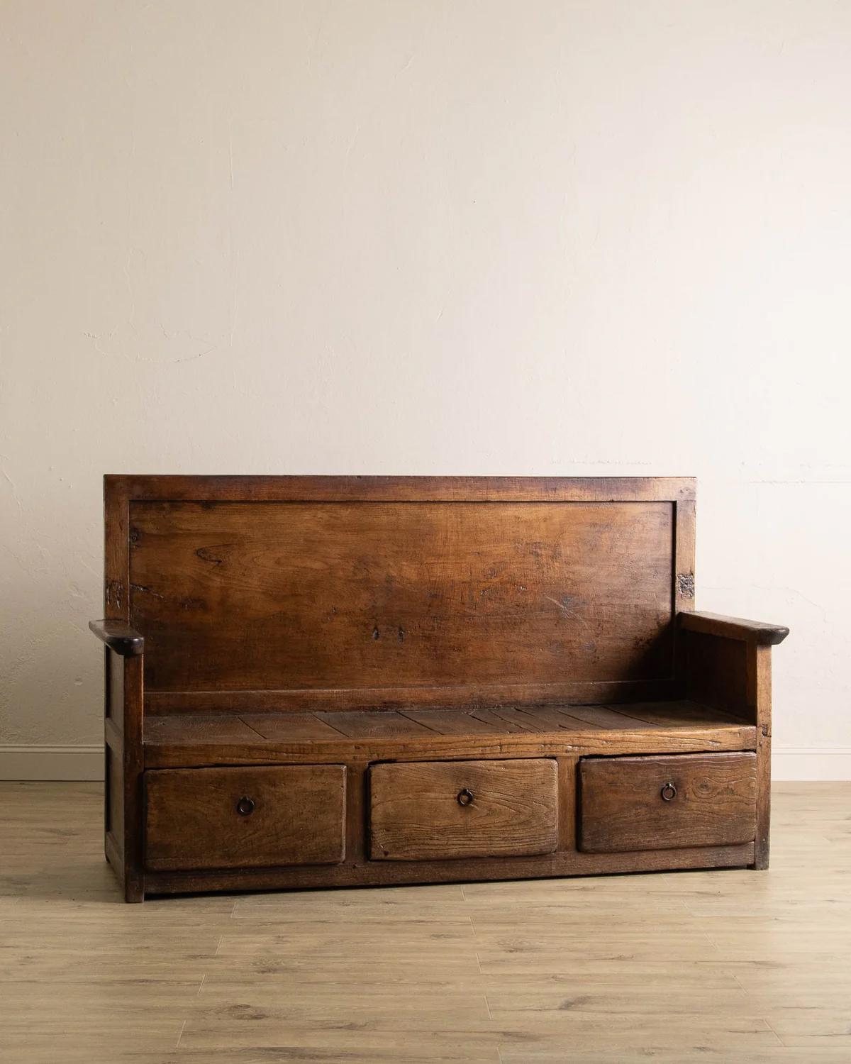 This 18th Century Dutch Oak Settle Bench is an impressive example of traditional craftsmanship, hand-carved from solid oak and designed with both beauty and utility in mind. The piece features three generously sized lower drawers, offering practical