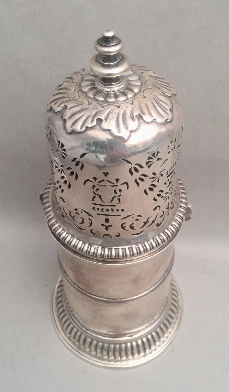 A large 1725 English sterling silver sugar shaker muffineer. Designed with finial, leaf motif around the top, pierced decorations, and a gadrooned base. Measuring 10 inches tall and 4 3/4 inches in diameter at base. Weighing 18.6 troy ounces.