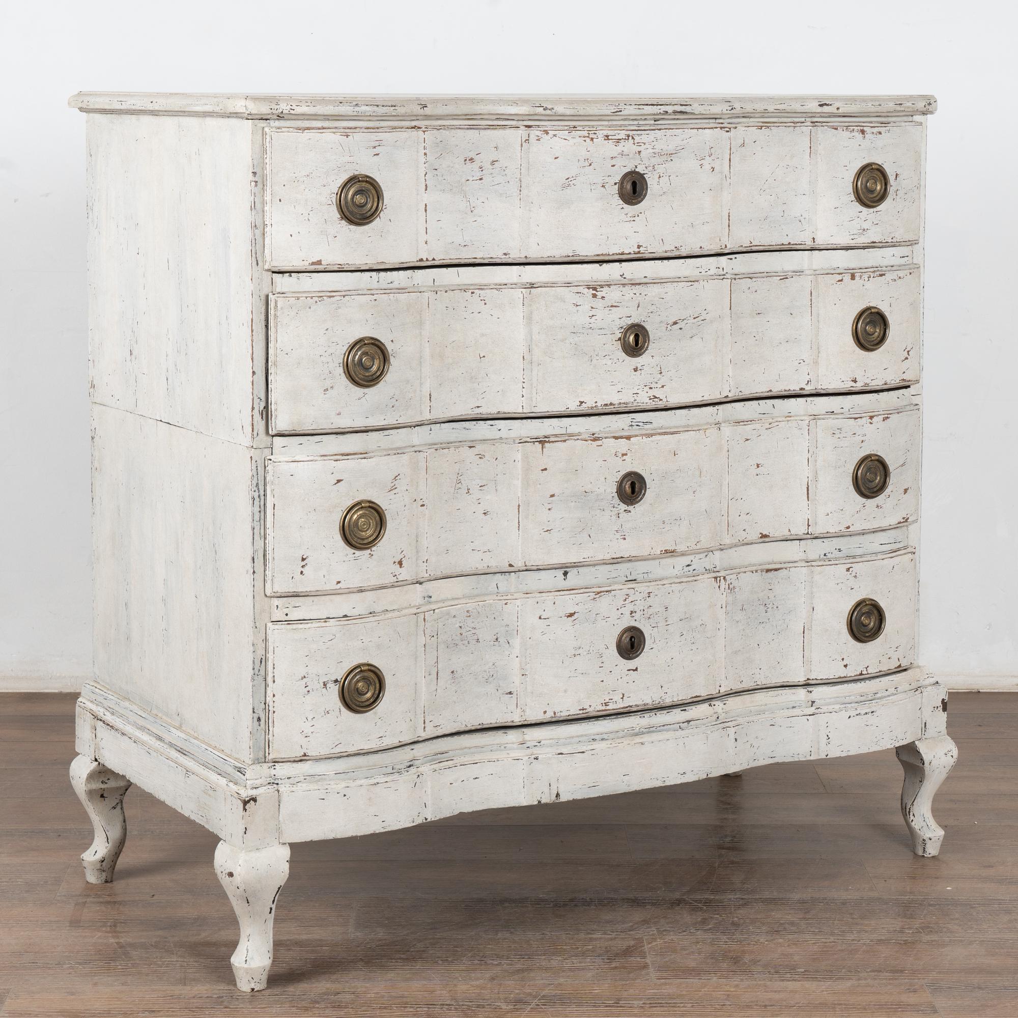 The antique white painted finish is captivating in this attractive large chest of four drawers resting on curved cabriole feet. While the paint is newer and professionally applied, it compliments the age, rococo style and serpentine curves of this