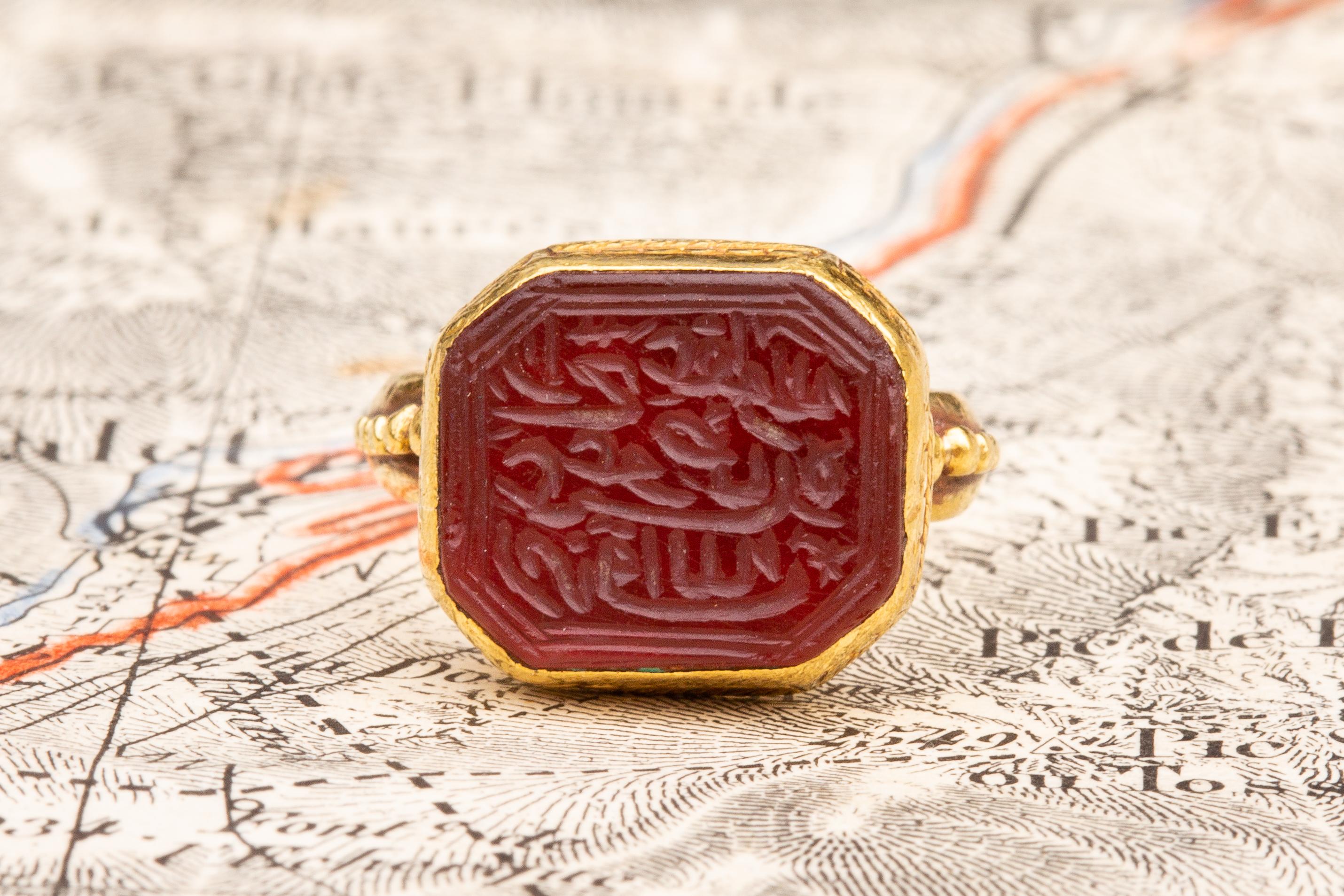 This superb Islamic gold ring dates to the the mid-18th century, circa 1760. It is set with an octagonal flat cut carnelian intaglio with bevelled edges. The stone is engraved with decorative Nastalīq calligraphy featuring stylised dots and stars,