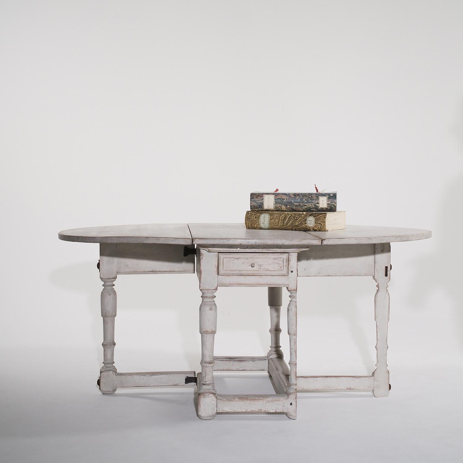 A light-grey, antique Swedish Gustavian drop-leaf table with one drawer, made of hand crafted painted Pinewood, particularized in the Neoclassical Greek style, in good condition. The half round Scandinavian dining table is supported by four round