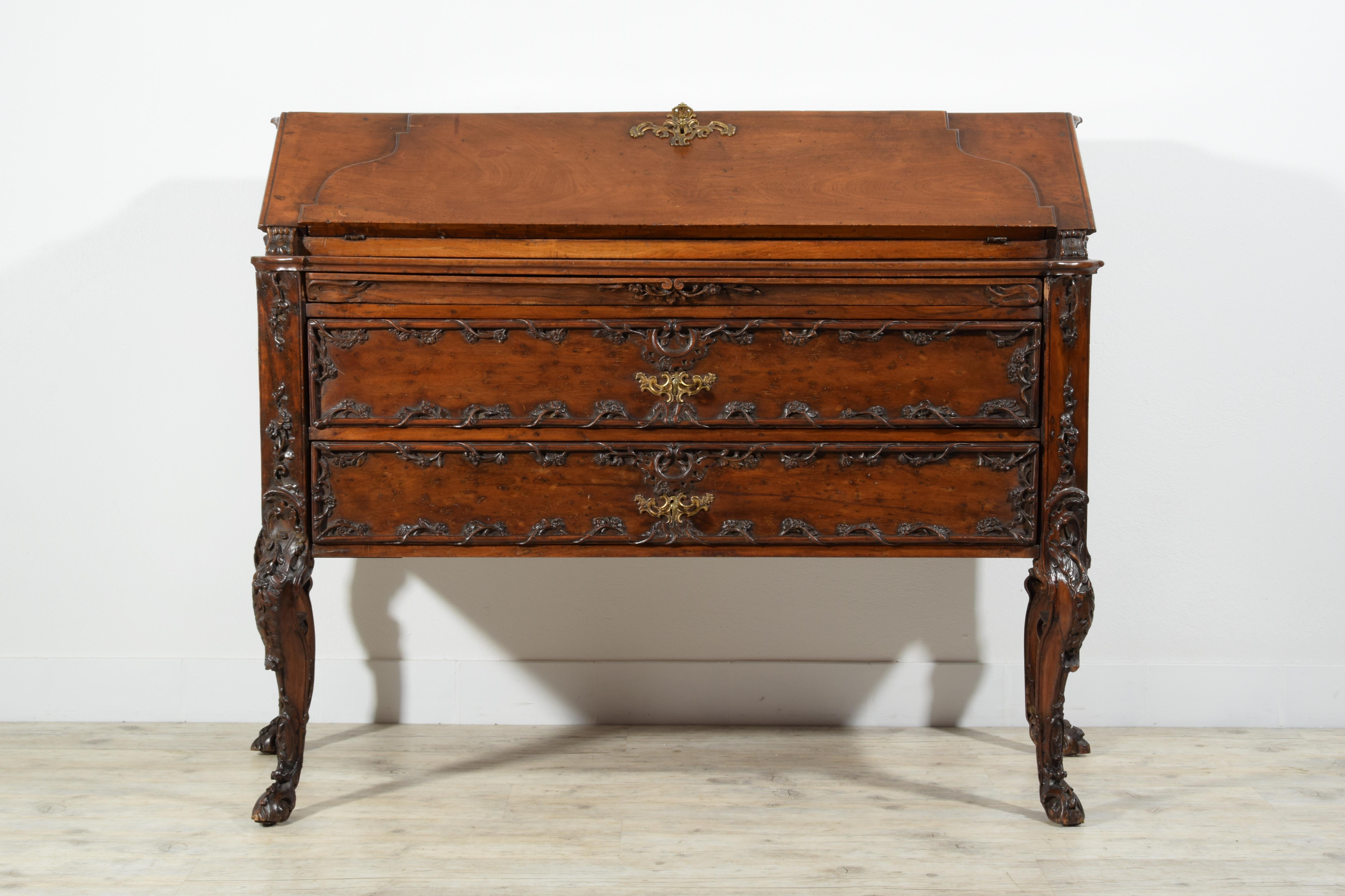 This elegant drop-leaf cabinet was made in the early eighteenth century in walnut wood finely carved with rocaille motifs. It has a particular patina of the carvings, slightly darker and brighter, which creates an effect similar to that of bronze.