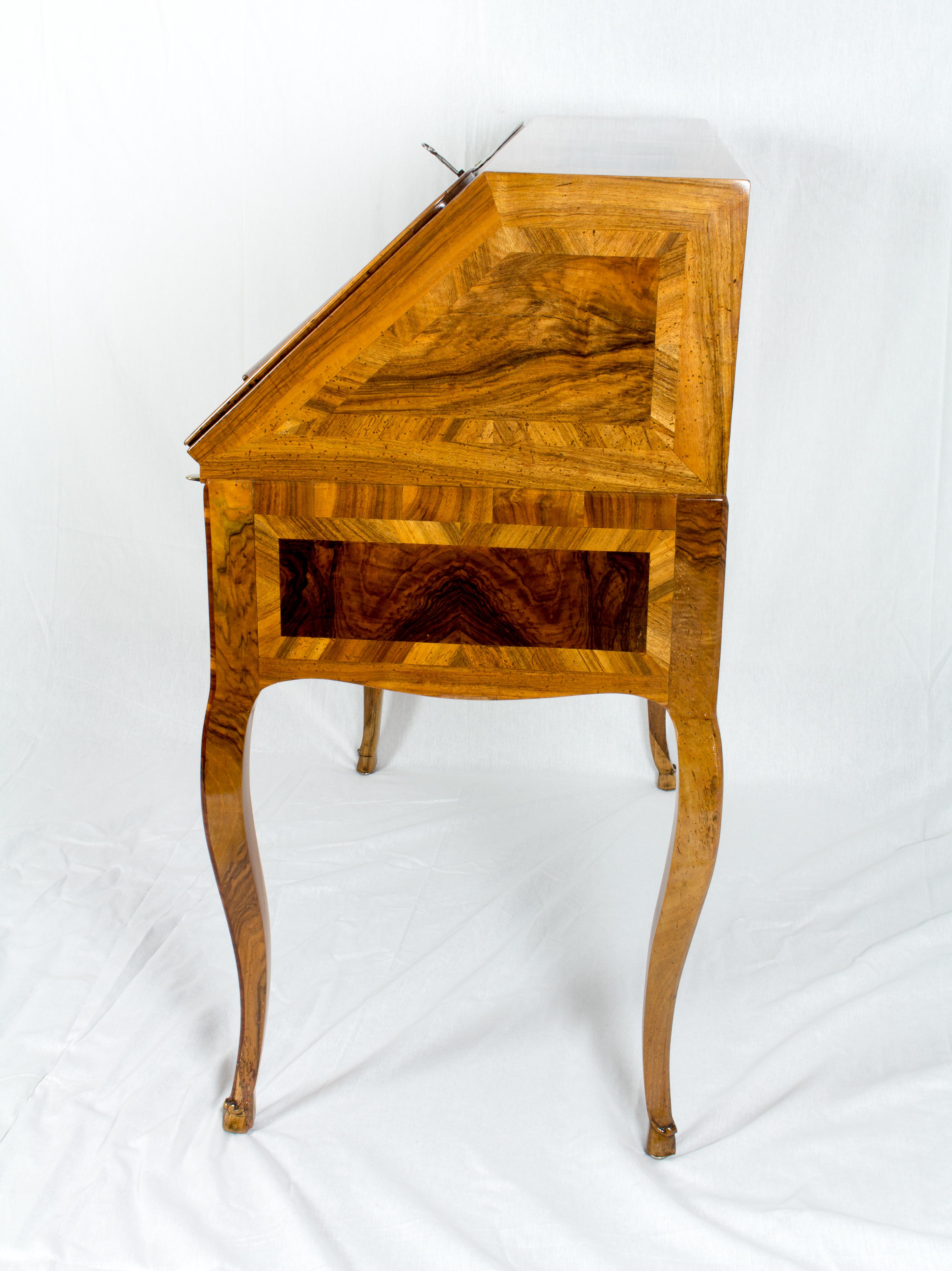 Der Schreibtisch stammt aus der Zeit um 1730 und ist mit einer schönen Intarsie aus verschiedenen Nussbaum- / Nussbaumwurzelhölzern auf einem Kiefernkorpus belegt.
Alle drei Schlösser sind original aus dieser Zeit, ebenso wie die Beschläge. 
Das