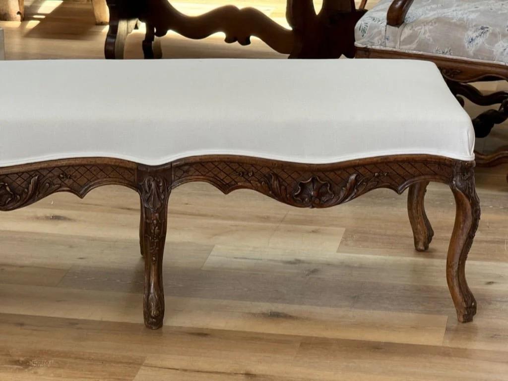 Banc Louis XV en hêtre du 18ème siècle avec restaurations.   Nouvellement tapissé en lin belge.  D'excellentes proportions pour être placées au bout d'un lit, s'adaptant aussi bien aux dimensions Queen qu'aux dimensions King.

