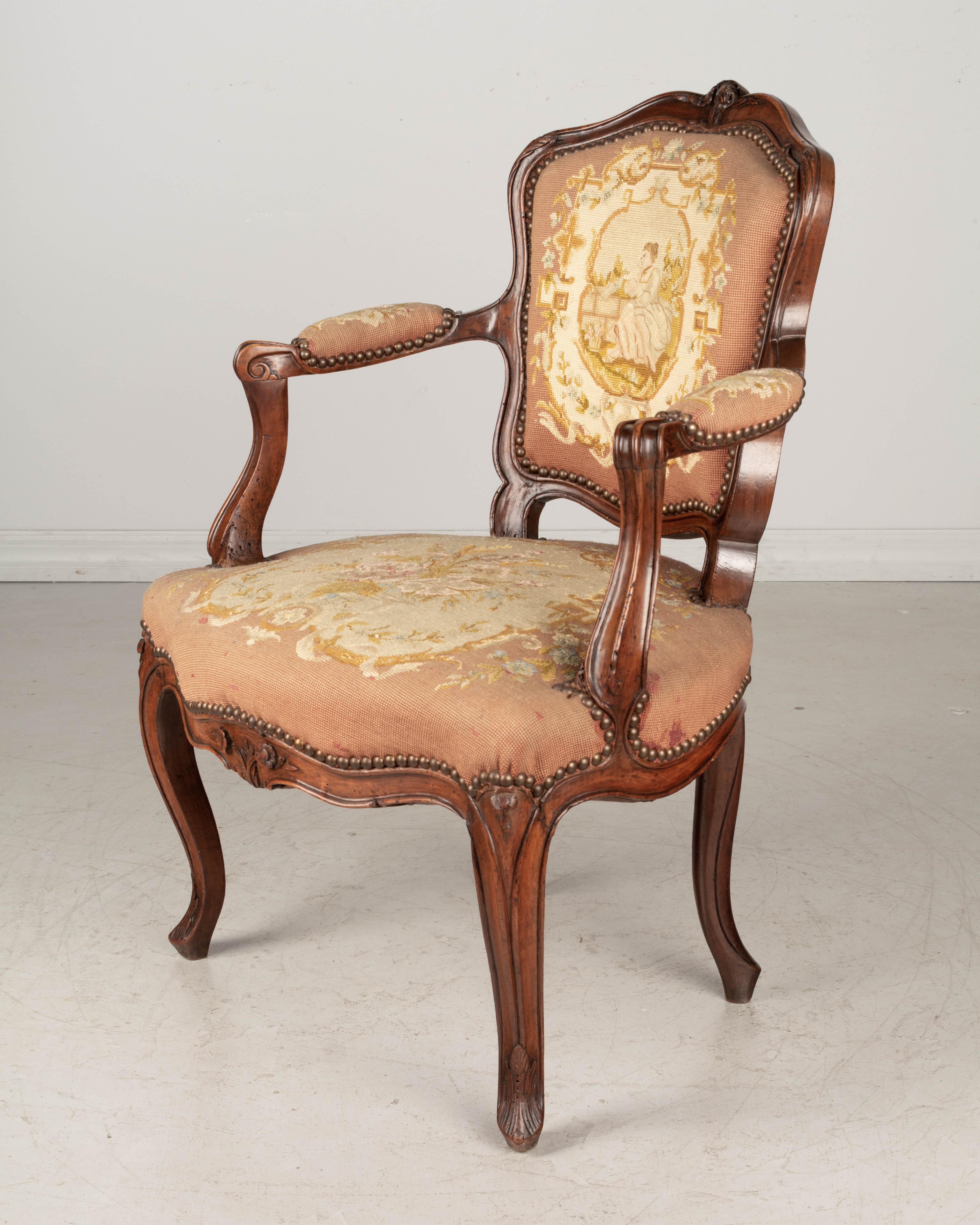 A small 18th century Louis XV French fauteuil, or armchair, with sturdy walnut frame and fine hand carved decoration. Upholstered in 19th century petit point tapestry. Pegged construction. This chair sits low to the ground with a seat height of 17