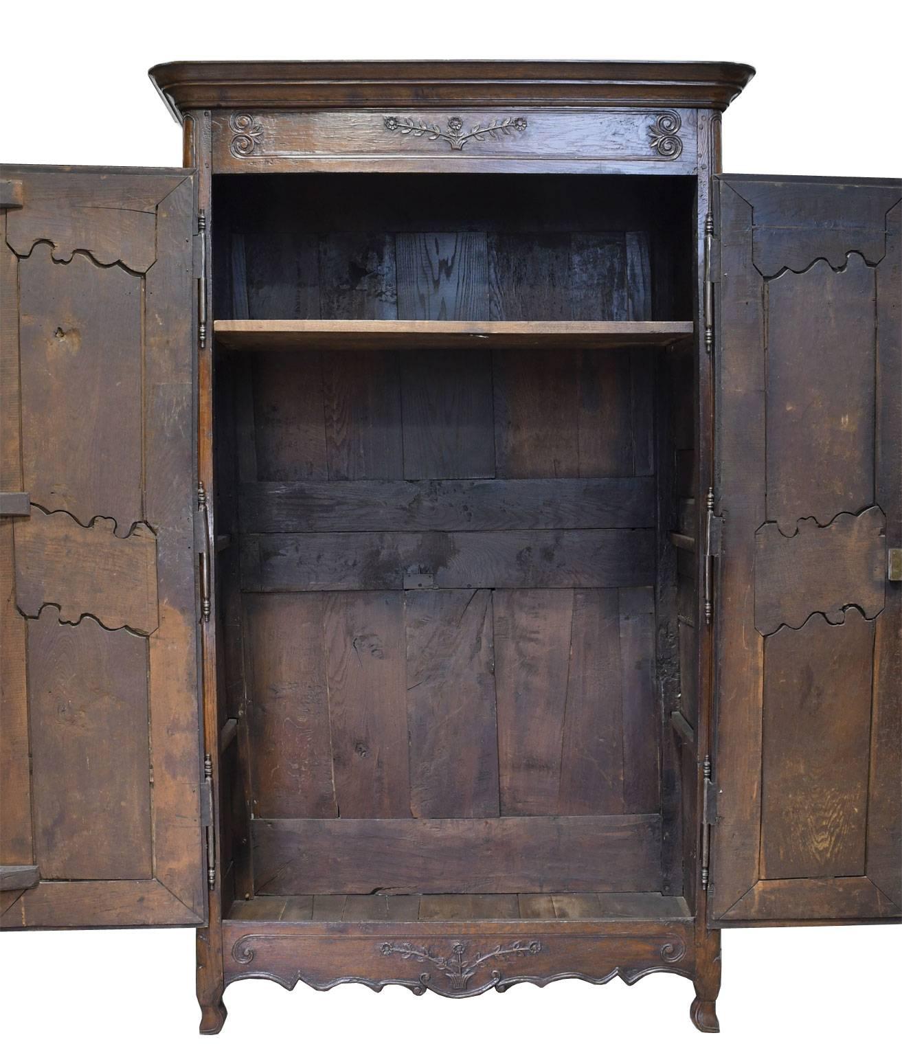 A lovely French armoire in oak with carved foliate and floral decorative elements on doors, crest and apron. Mortice and tenon construction with wooden pegs, befitting the period. Oak has a rich dark patina, with carvings the result of a reduction