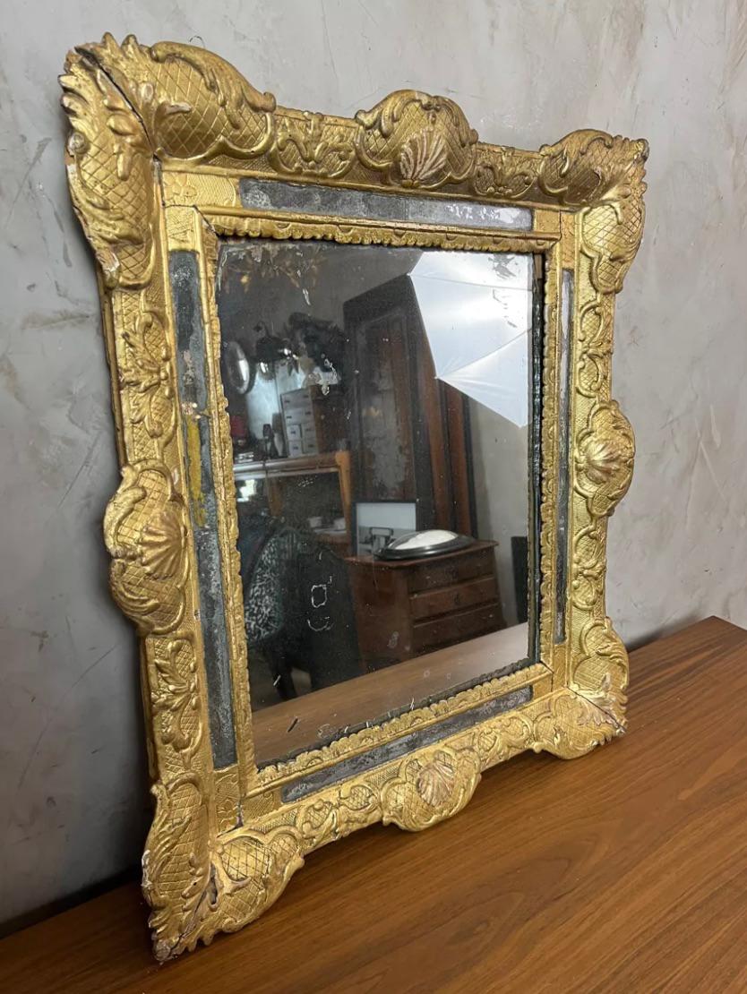 Antique Louis XV period mirror. Its gilded frame is richly decorated with floral motifs, stylized shells, and scrolls, typical of the classical and baroque eras. The mirror glass shows signs of age, adding unmatched charm and authenticity.