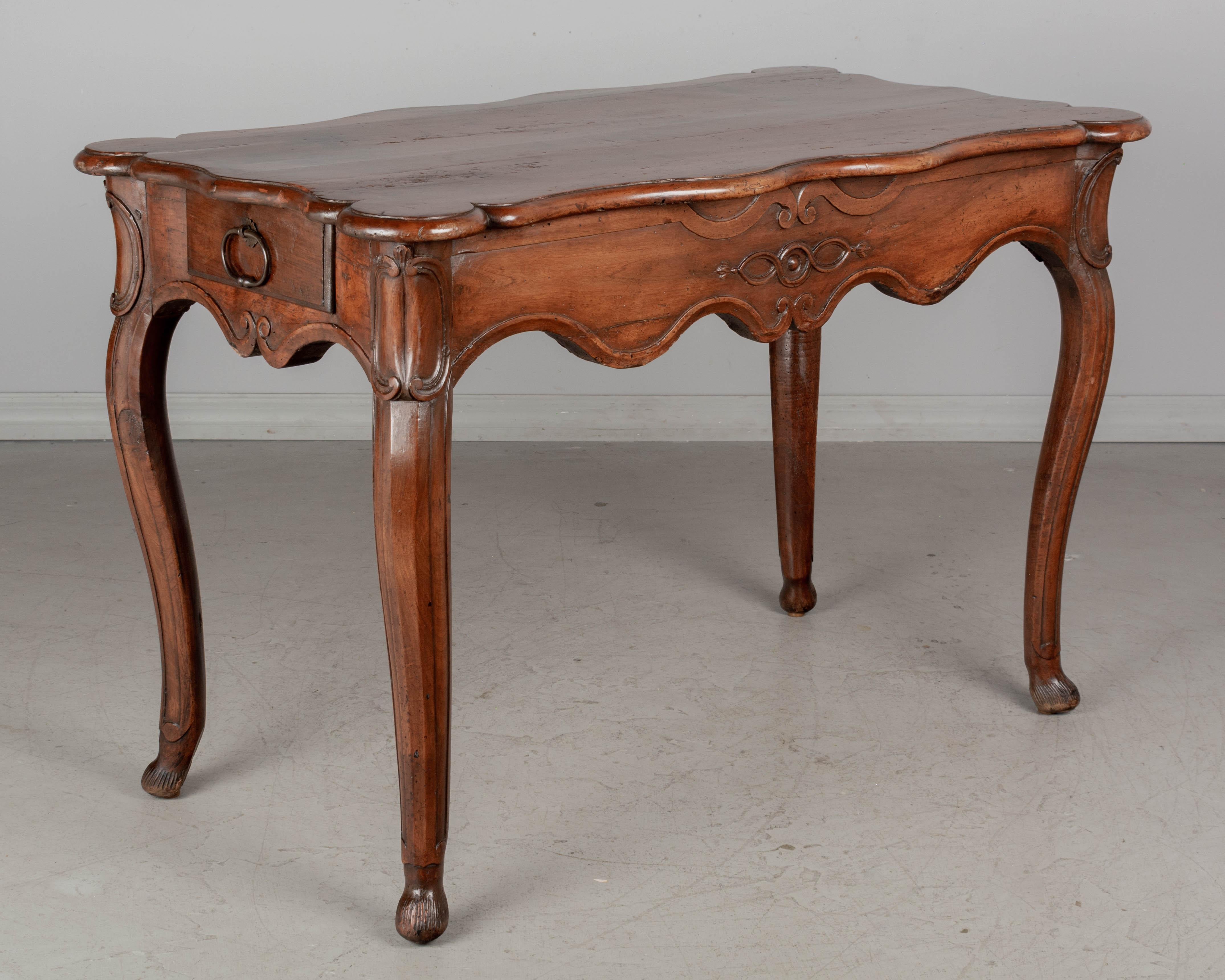 An 18th century French Louis XV table from Provence. Made of solid walnut with deep hand-carved apron and thick cabriole legs. Two dovetailed drawers, one on each side, each with iron loop pulls. Shaped top with rounded corners. Beautiful character