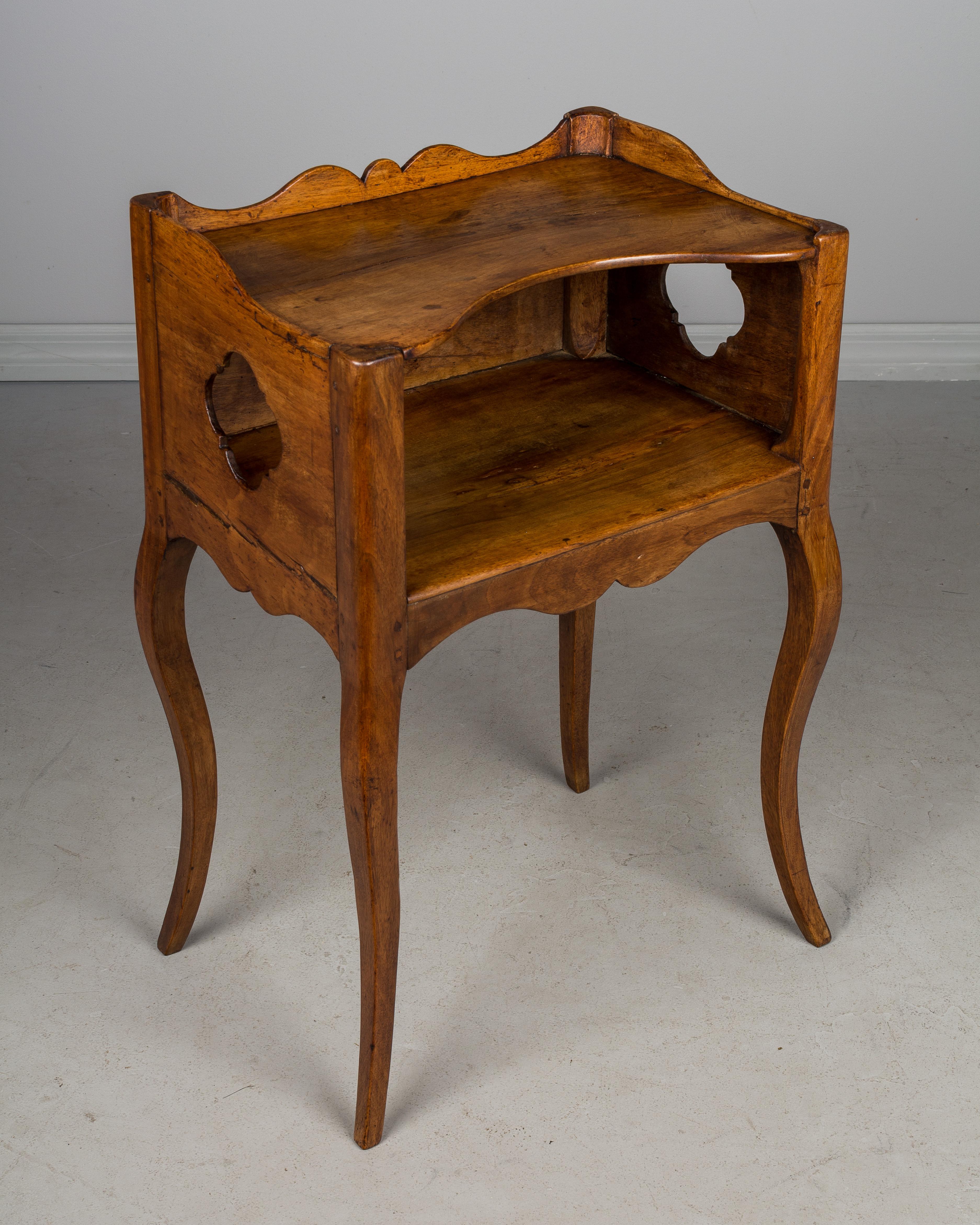 A late 18th century Louis XV country French side table or nightstand made of solid walnut, with a pierced quatrefoil shape cut-out on the sides and on the back. Scalloped apron and gallery surrounding the upper shelf. Slender curved legs. A sturdy,