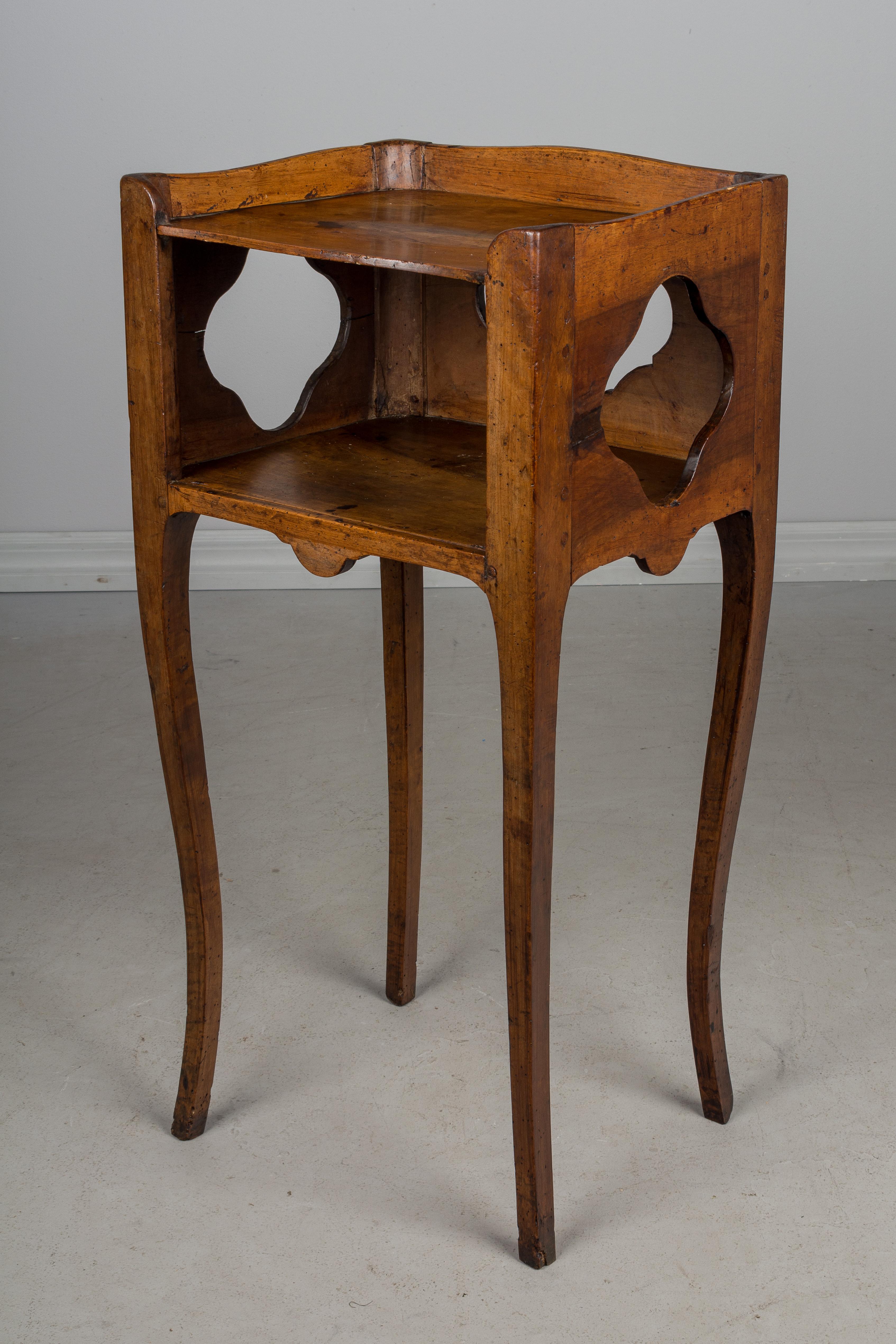 A late 18th century Louis XV country French Provencal side table or nightstand made of solid walnut, with a pierced quatrefoil shape cut-out on the sides and on the back. Scalloped apron and gallery surrounding the upper shelf. Slender curved legs.