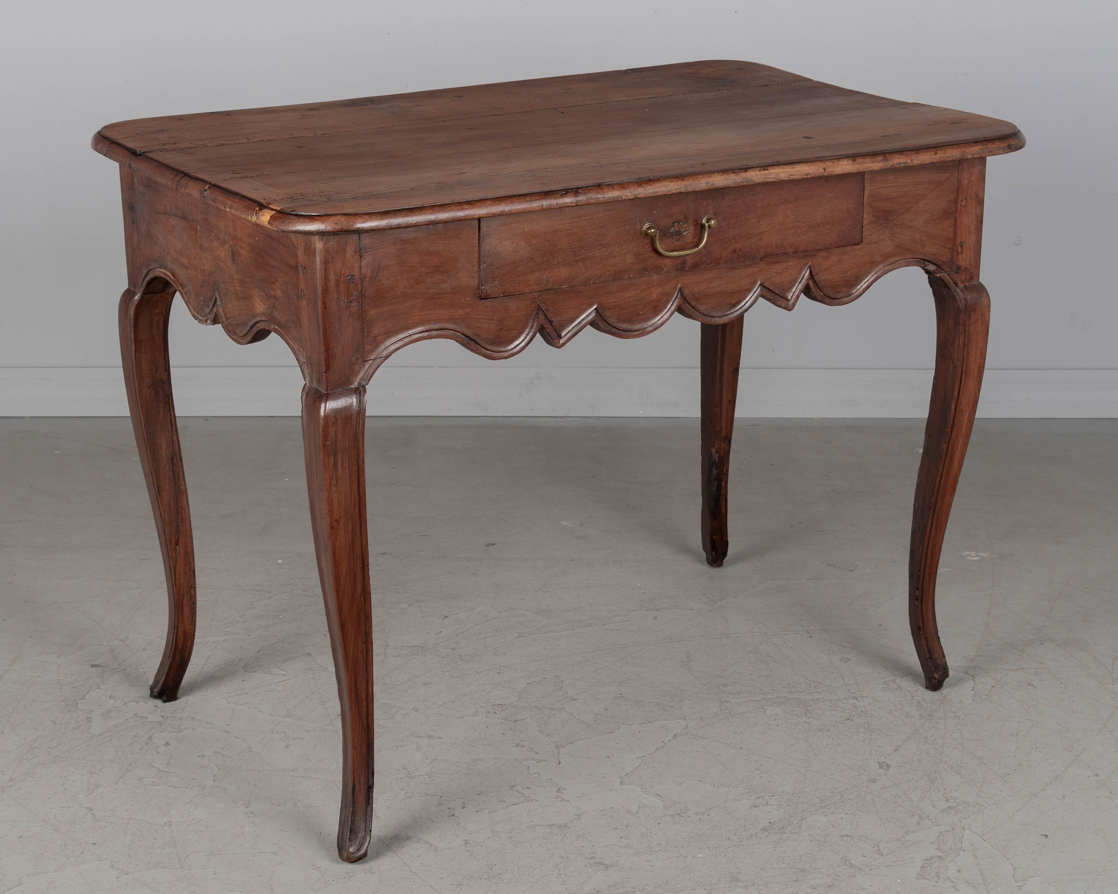 Tavolino o piccolo scrittoio Luigi XV del XVIII secolo in ciliegio massiccio con grembiule smerlato e gambe ricurve. Cassetto singolo a coda di rondine con tiretto in ottone. Restauro in cima. Circa 1780-1800.
Dimensioni: 37,5