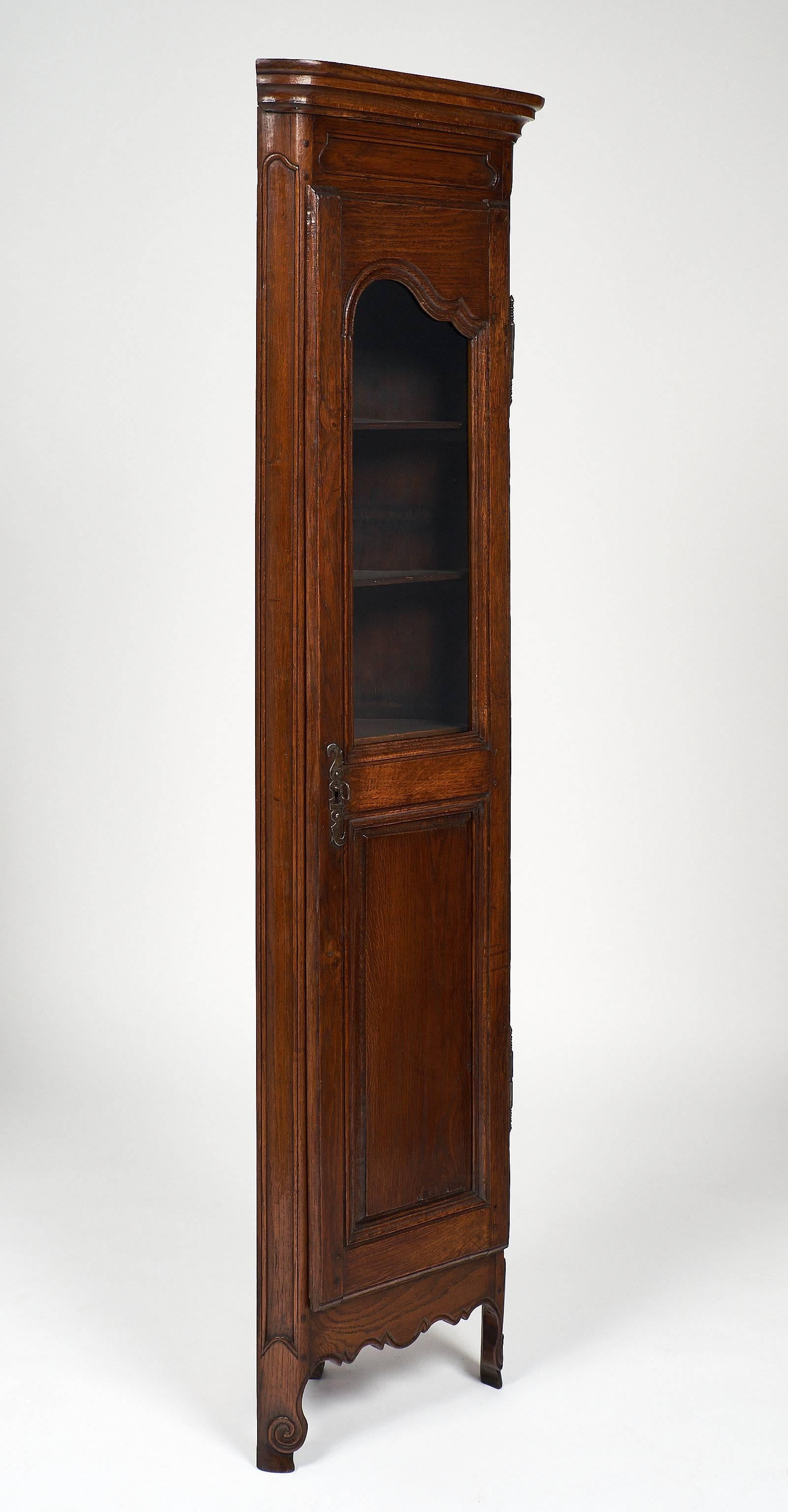 A rare Louis XV style 18th century corner cabinet with a single glass door. The oak wood is hand-carved and patinated, featuring cabriole legs with a scalloped apron. The lock and key are in working condition.