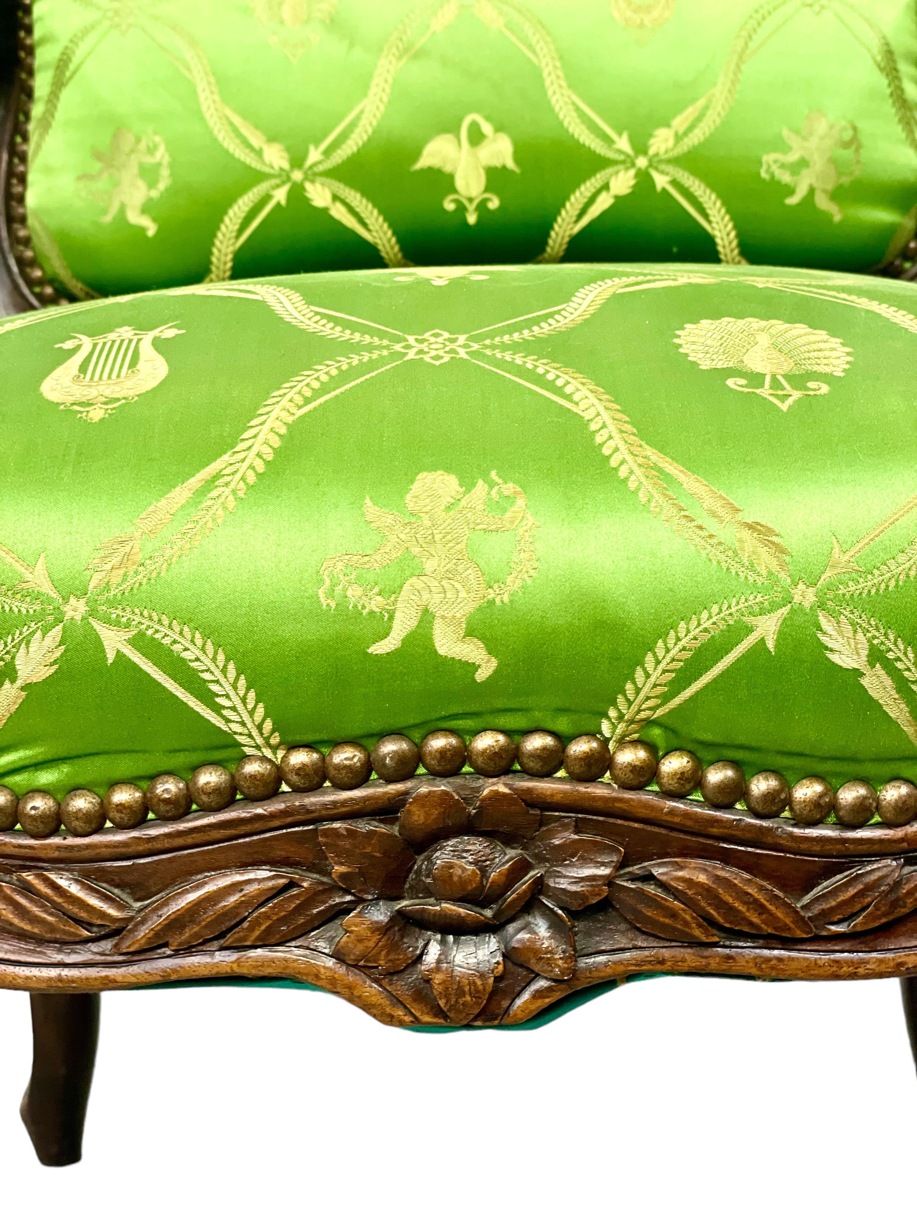 A wide and comfortable Louis XV style fauteuil 'à la reine', hand carved in the 18th century and featuring exquisite green silk upholstery woven with neoclassical motifs of lyres, cherubs, peacocks and swans. The shoulder-high back rest and