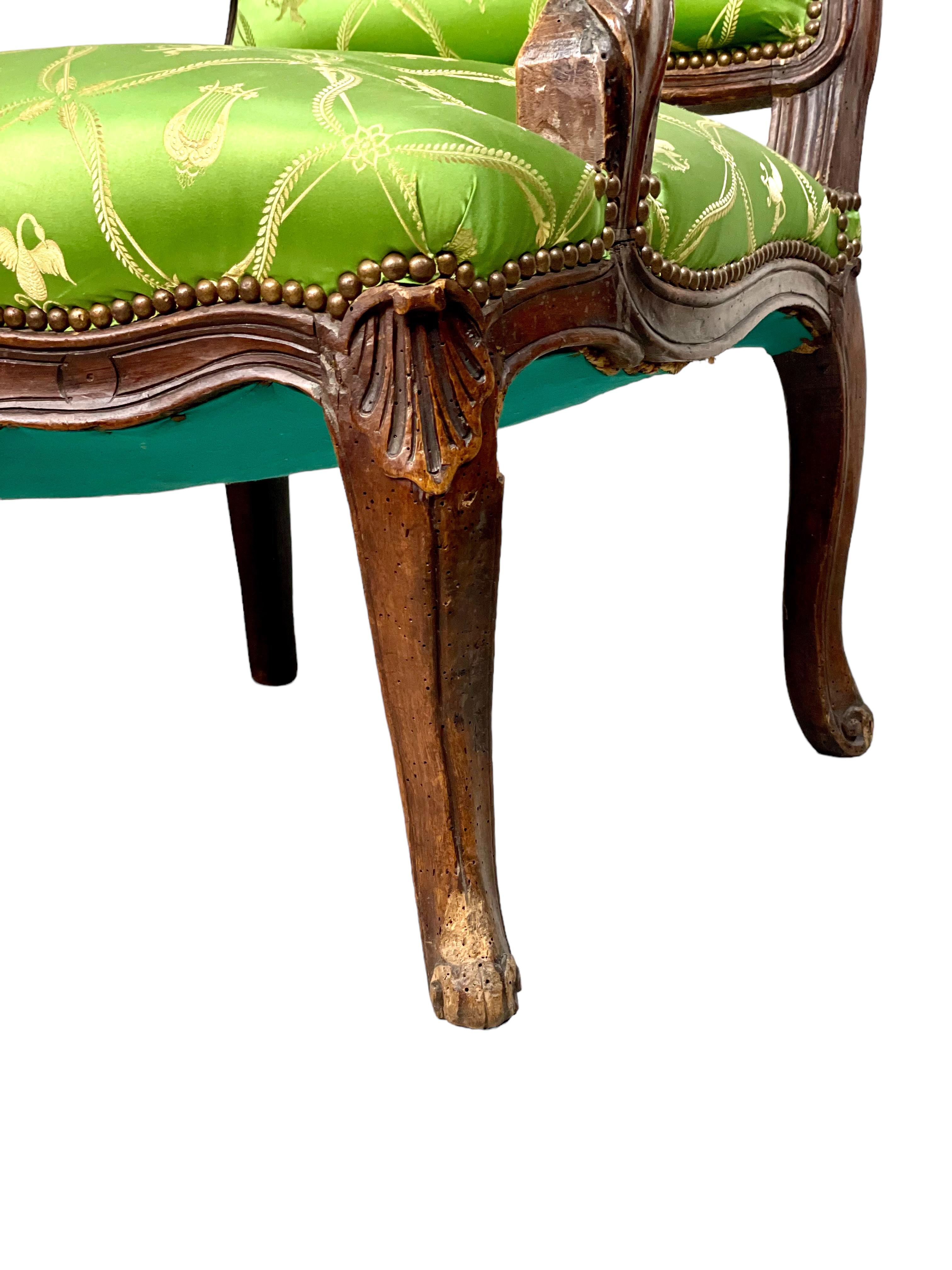 A wide and comfortable Louis XV style fauteuil, hand carved in the 18th century and featuring exquisite green silk upholstery woven with neoclassical motifs of lyres, cherubs, peacocks and swans. The shoulder-high camel back rest and arm rests are