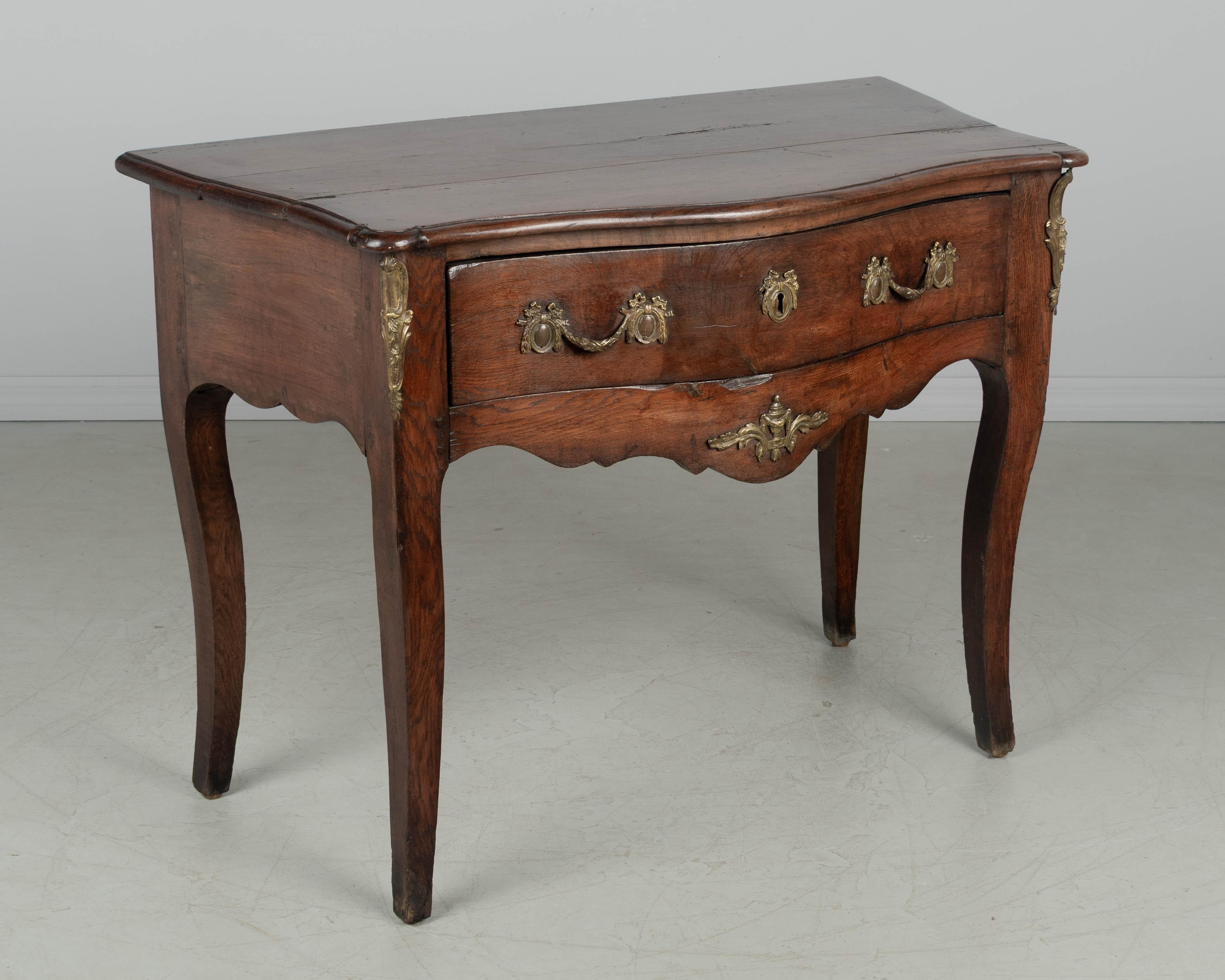 Consolle provenzale francese del XVIII secolo in stile Luigi XV con fronte a serpentina, lati curvi e ampio cassetto a coda di rondine. Realizzato in rovere massiccio con piano in noce. La ferramenta in bronzo fuso è dell'epoca ma potrebbe non