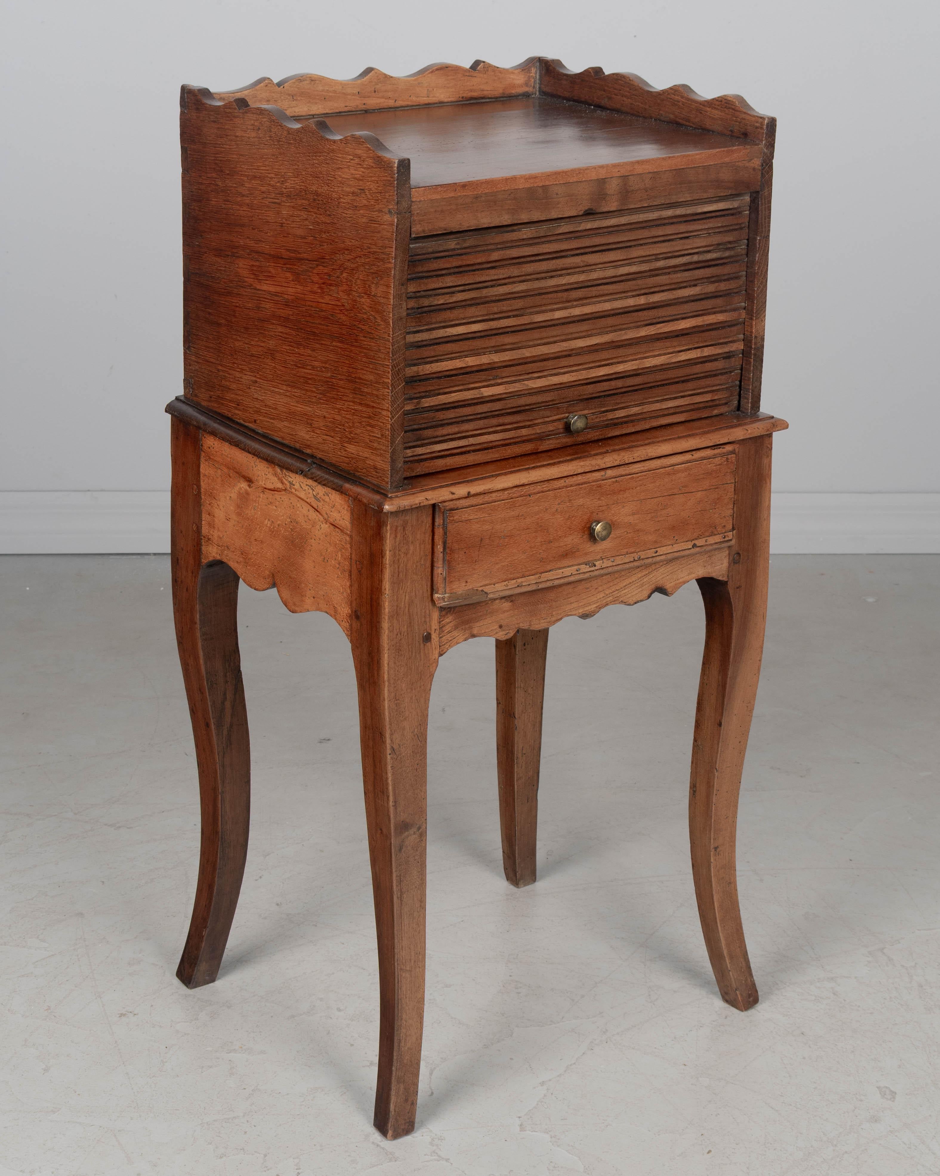 A late 18th Century Louis XV style Country French table de chevet, or bedside table, made of solid walnut and oak with a tambour door and a small dovetailed drawer. Scalloped apron and gallery and sturdy curved legs. Good craftsmanship using