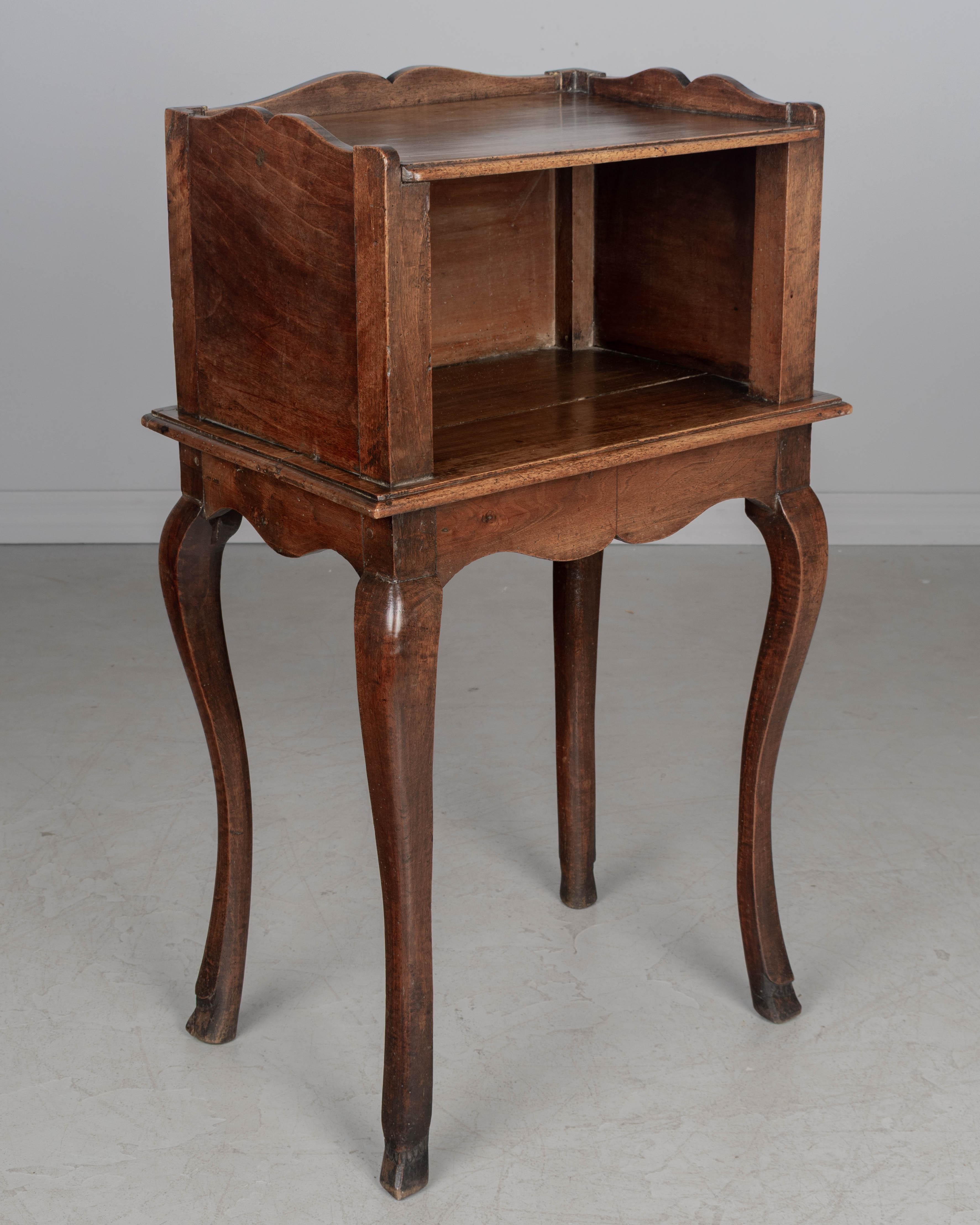 A late 18th Century Louis XV Country French table de chevet, or bedside table, made of solid walnut. Open niche with scalloped apron and gallery. Sturdy cabriole legs ending in deer hoof feet. Good craftsmanship using pegged construction. Waxed