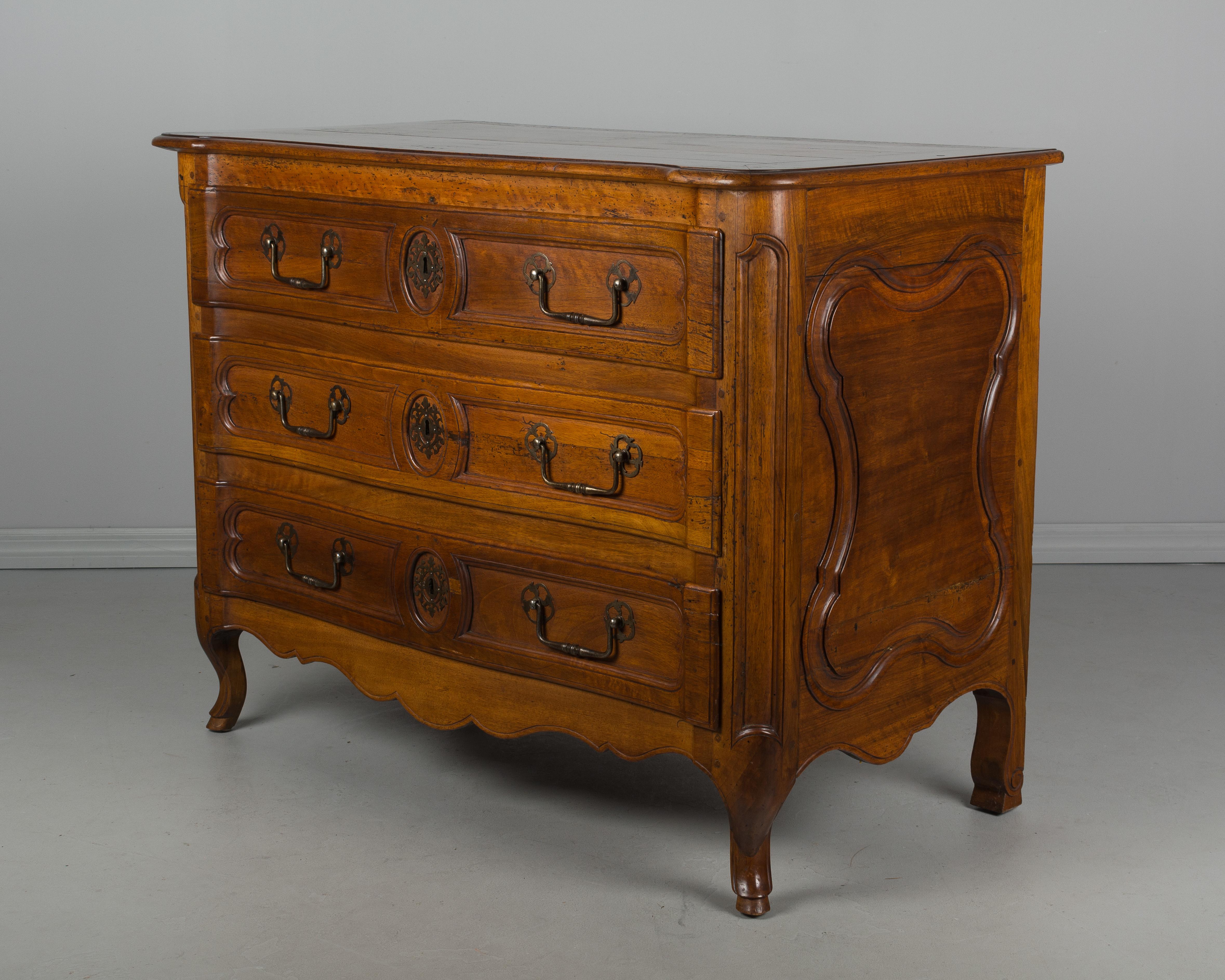 A late 18th century French Louis XV style walnut commode from Lyon. Slightly curved front and subtle carved details including shaped side panels and a scalloped apron. Iron hardware is as found. Locks are present, but there is no key. Large