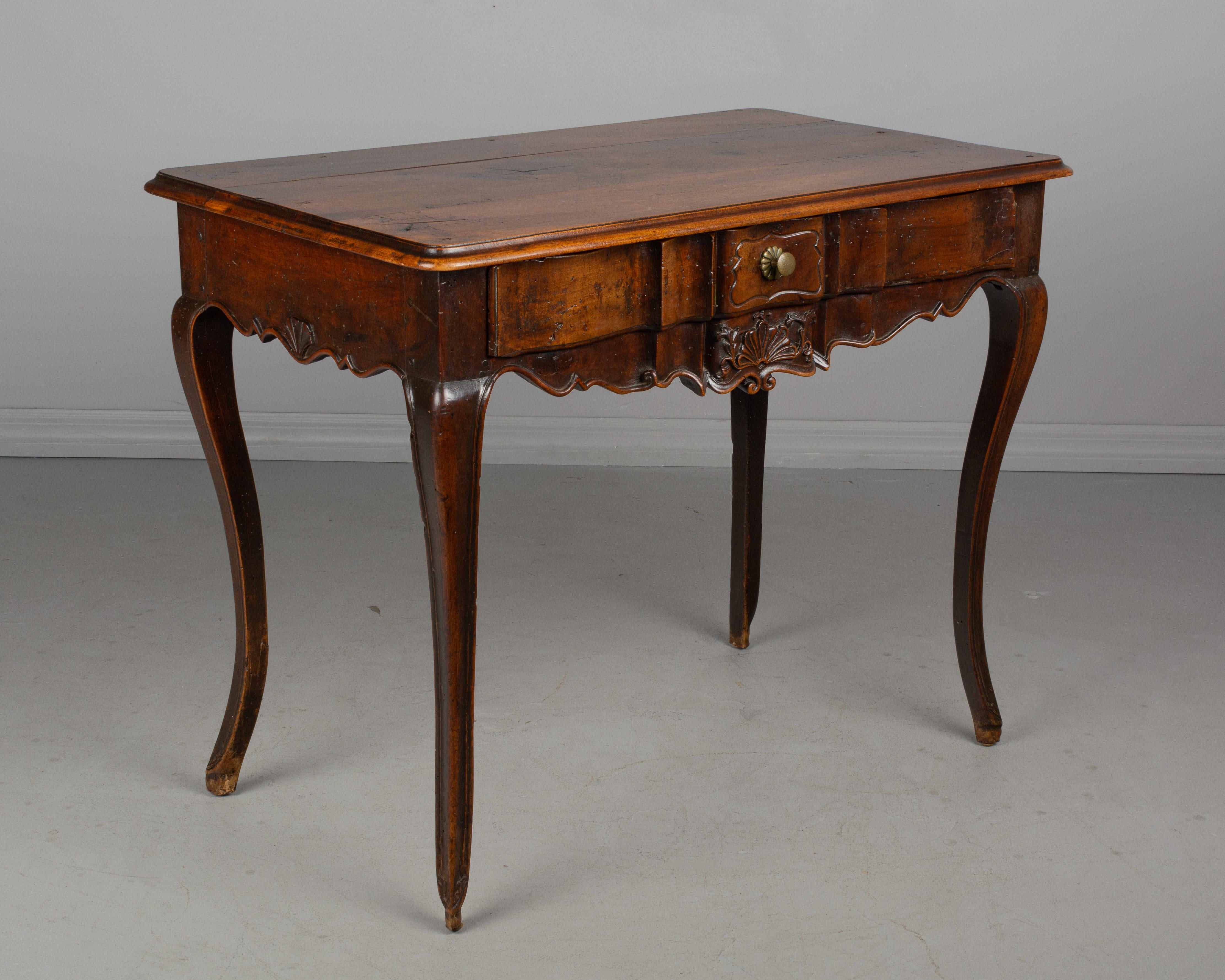 A late 18th century French Louis XV style writing table, or side table from Provence. Made of solid walnut with arbalete front, scalloped apron and hand carved shell motif. Dovetailed drawer with brass knob. Pegged construction. Waxed patina.