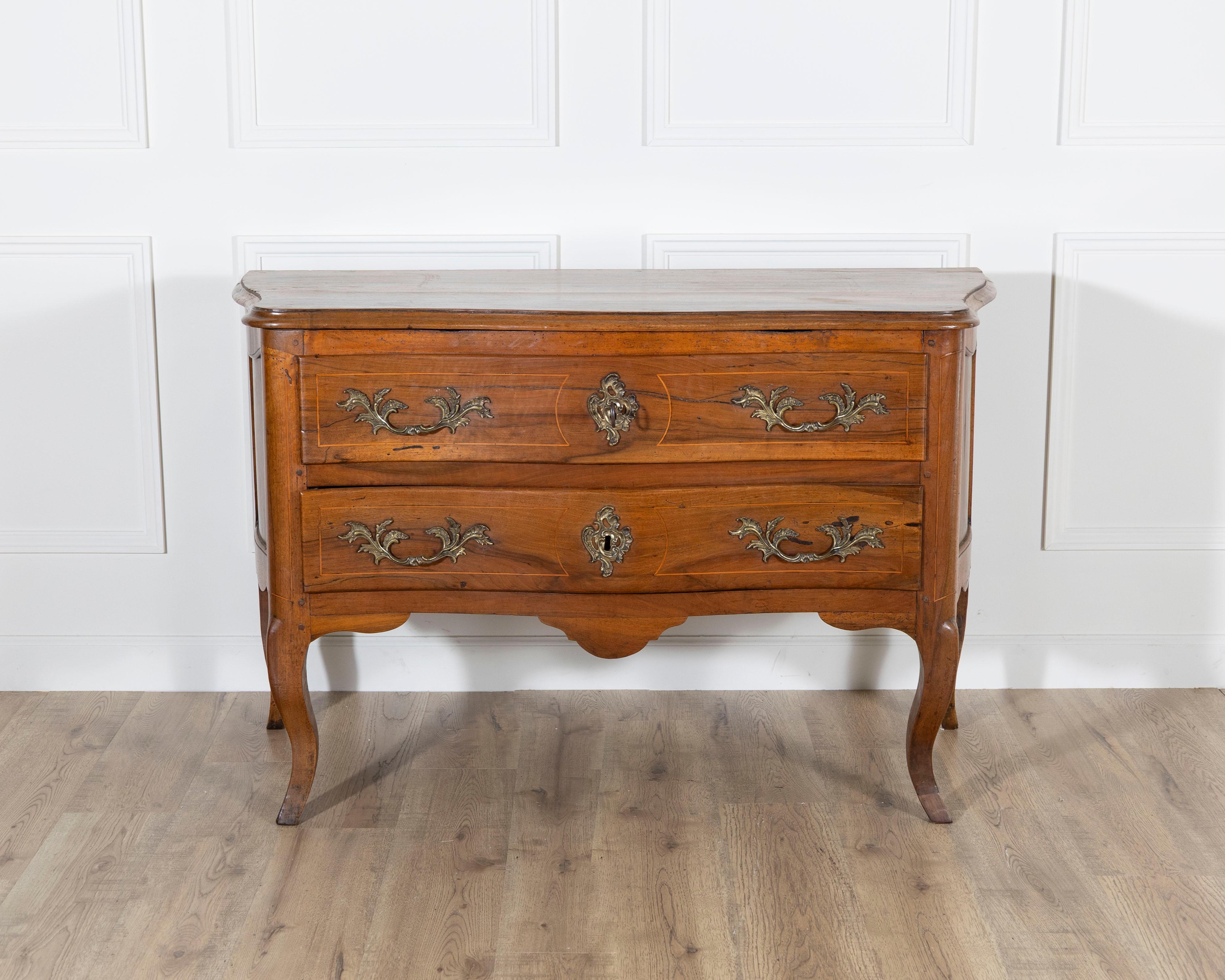 An elegant Louis XV period chest of drawers from the 18th century, crafted in solid walnut and distinguished by its graceful curves on three sides. The commode features a beautifully serpentine front, opening to two spacious drawers with carved