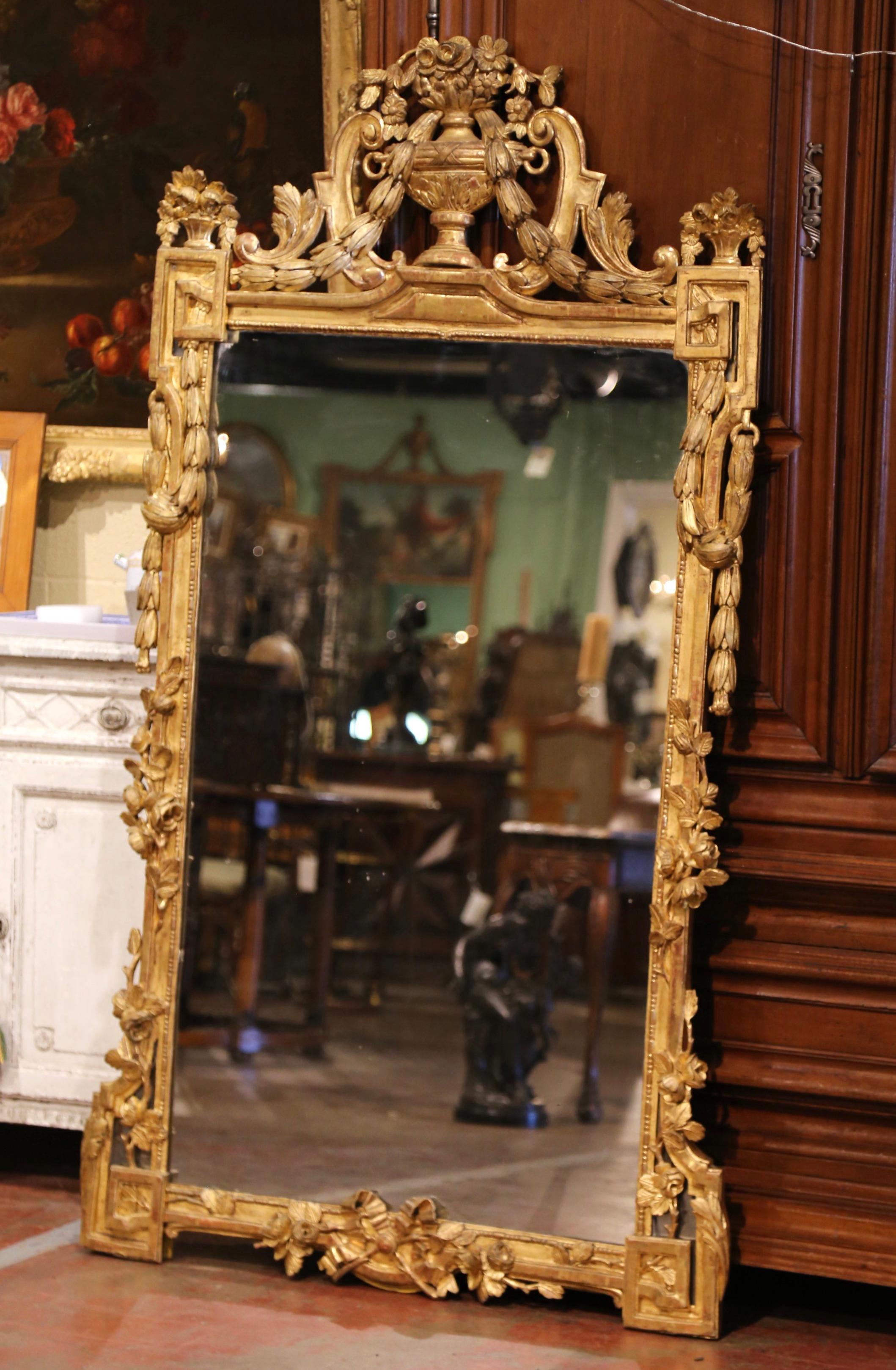 This important antique gilt mirror was crafted in Paris, France, circa 1780. The tall wall decor features a large cartouche at the pediment decorated with carved center vase, flanked with floral and swag motifs at the ends. Both sides are