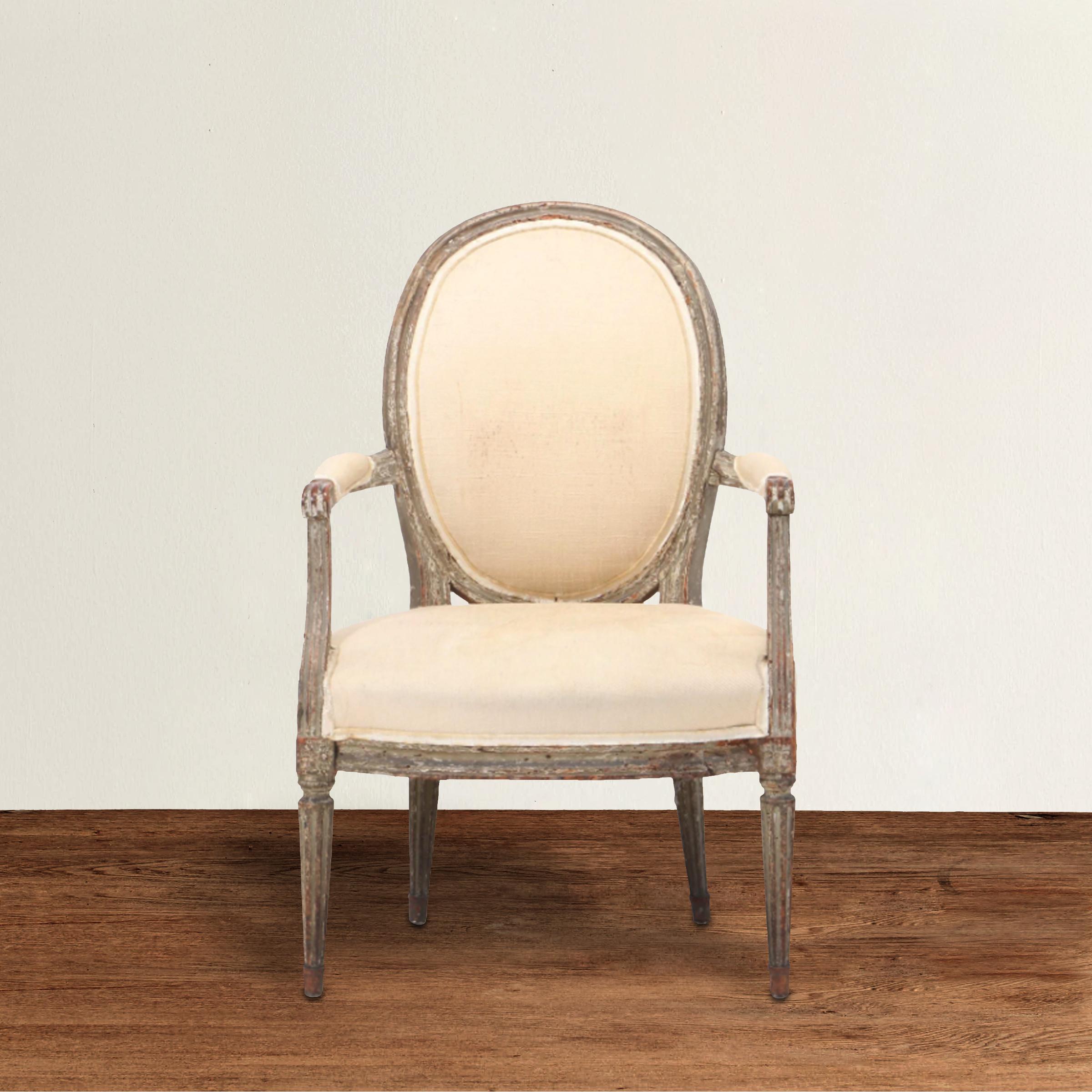 A wonderful 18th century French Louis XVI period fauteuil armchair with a large oval back, a generous wide seat, and tapered fluted legs. Chair retains traces of its original gray paint. Upholstered in a neutral canvas with tape trim, but with