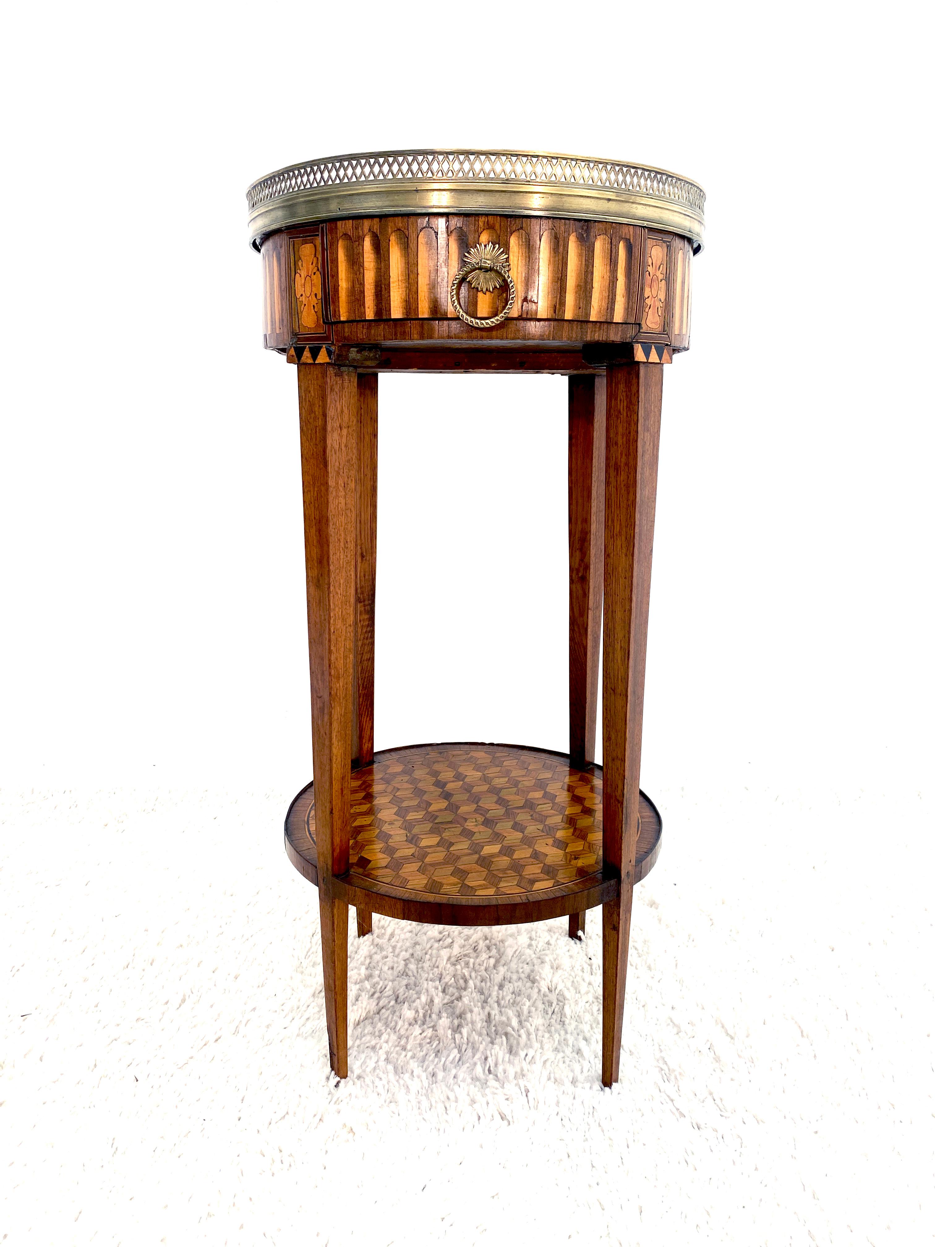 A very attractive Louis XVI period French guéridon table with a brass gallery encompassing a white marble top. Extensive marquetry veneer work throughout the perimeter and lower shelf. The table rests on tapered legs with one center drawer fitted