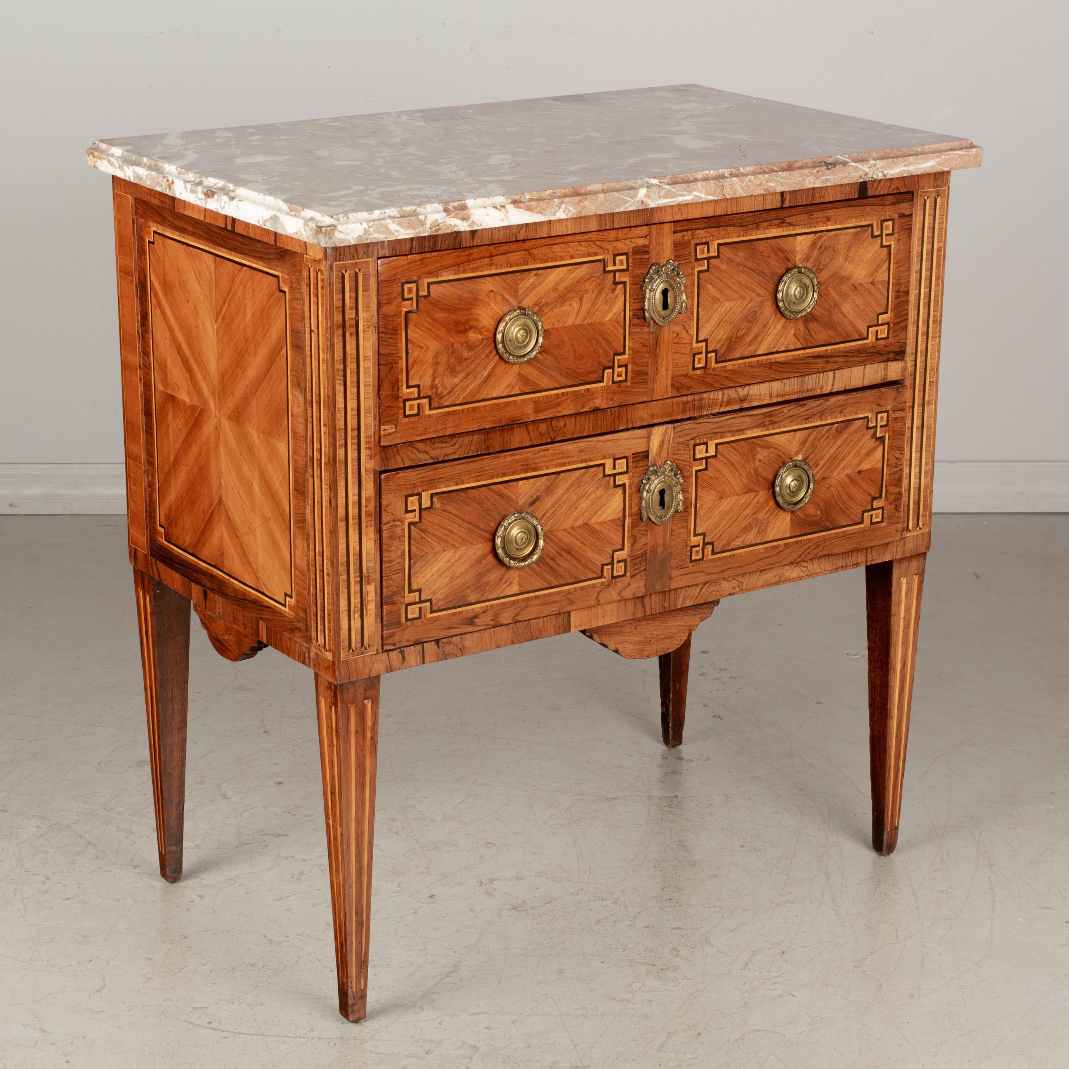 An 18th century French Louis XVI marquetry commode inlaid with veneers of mahogany, walnut and rosewood. Original Languedoc marble top. Two dovetailed drawers with original cast bronze hardware. Locks are present, but no keys. Slender tapered legs. 