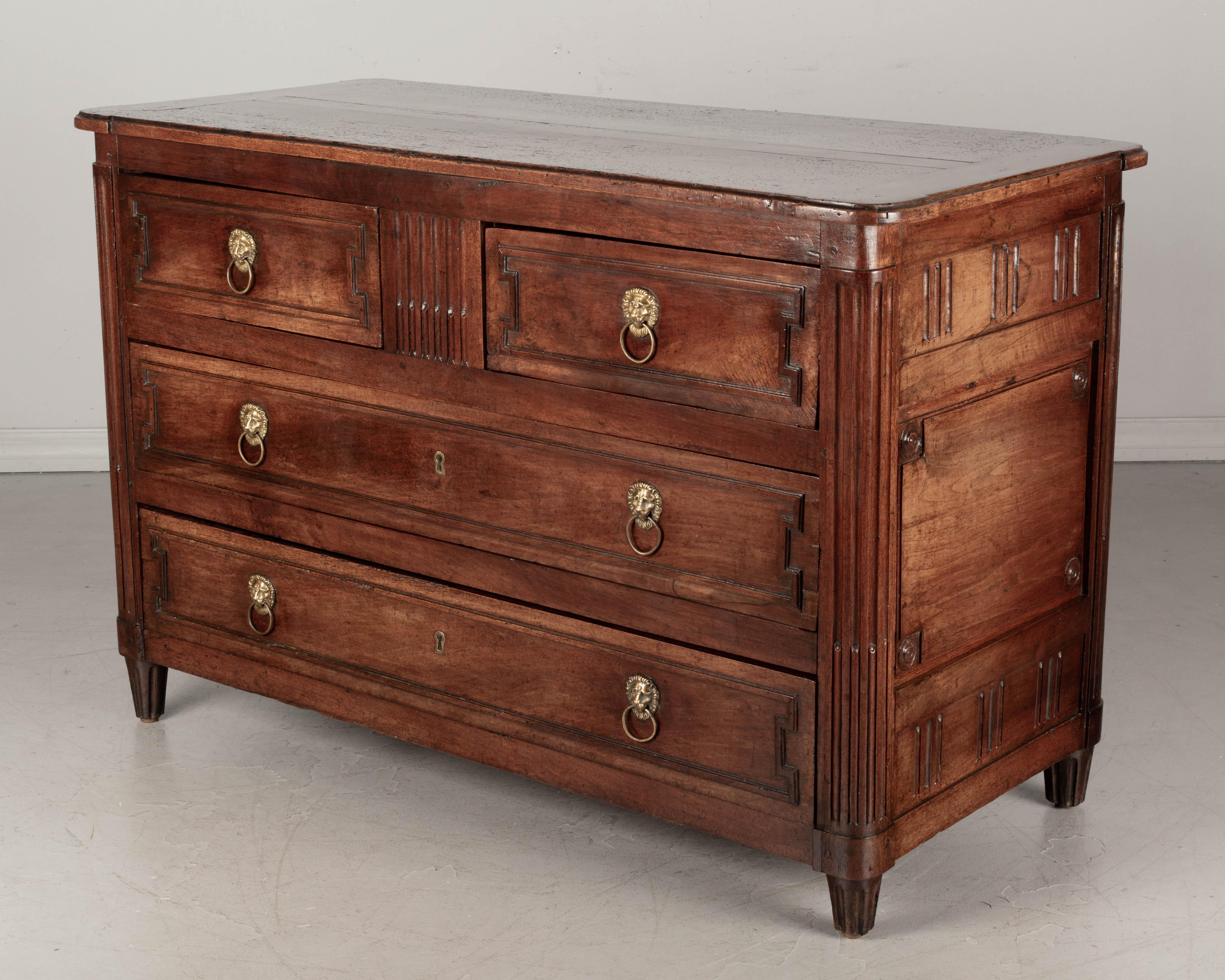 An 18th century French Louis XVI period commode, or chest of drawers, made of solid walnut. Three panels on the sides, rounded fluted corners and short tapered legs. Four dovetailed drawers with cast brass lion head ring pulls. The interior of the