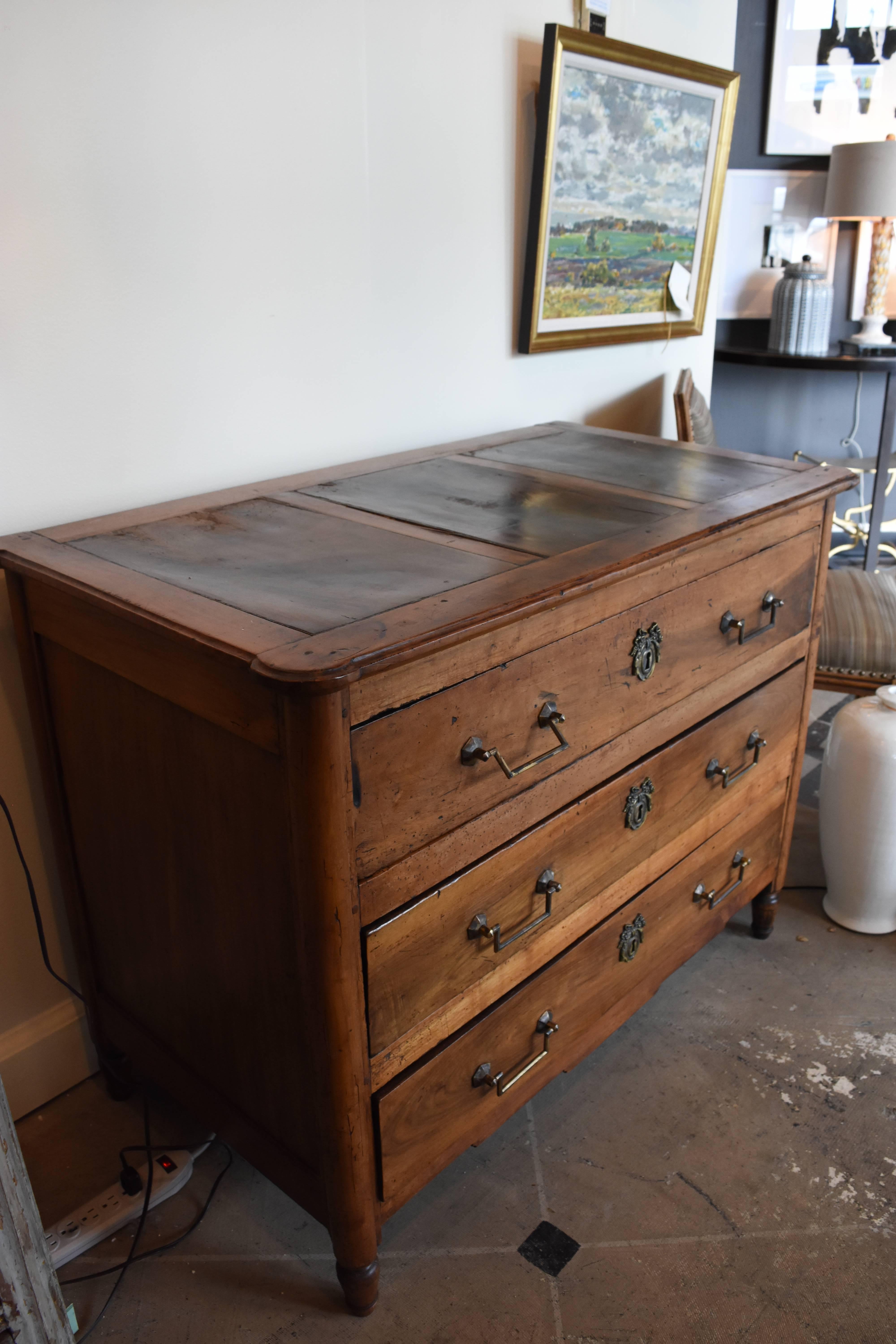 This late 18th century Louis XVI style walnut commode has a beautiful aged patina. It has three functional drawers of dovetail construction which boast bronze drawer pulls and escutcheons that feature a Classic Louis XVI knotted ribbon motif. The