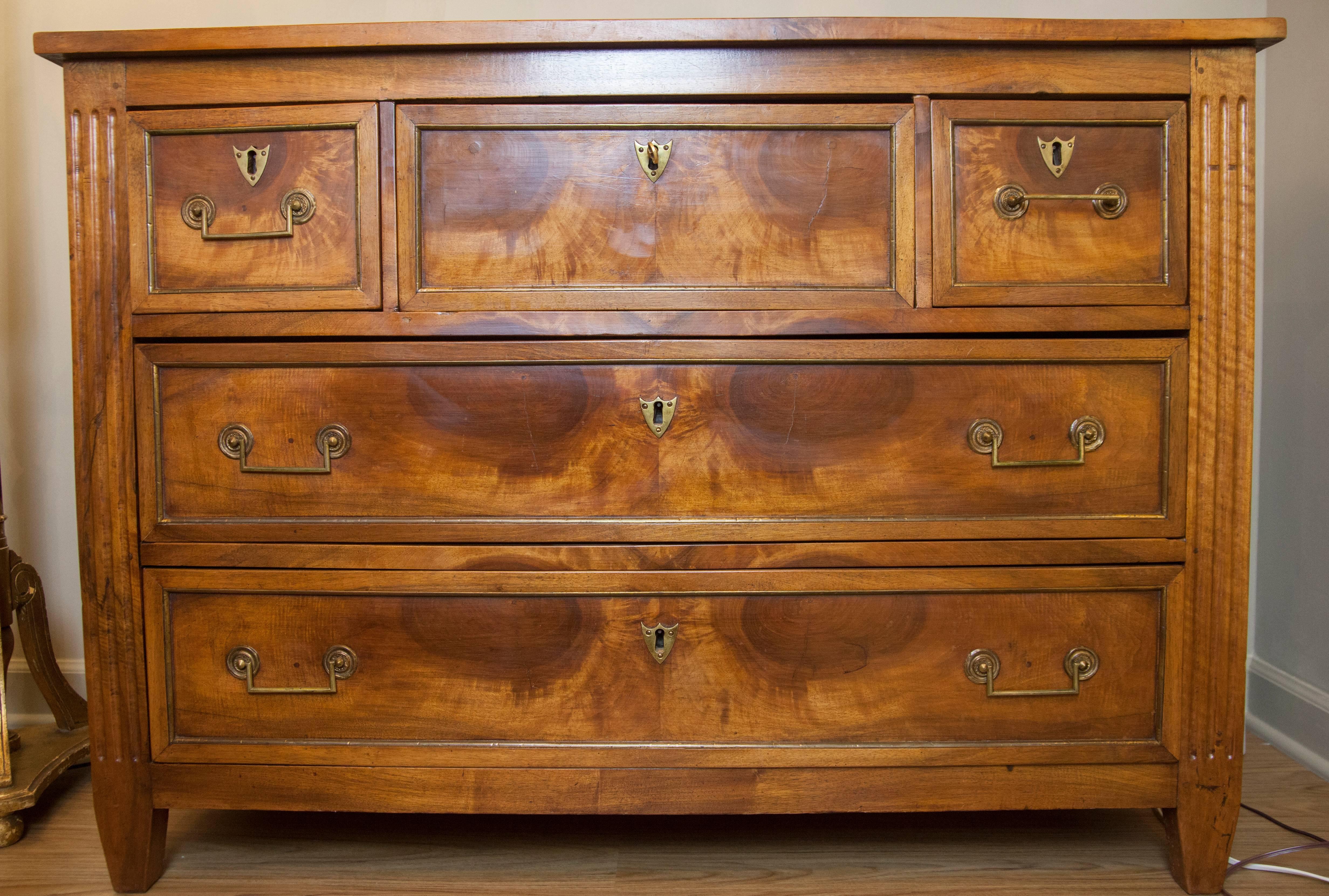 This 18th century Louis XVI style walnut commode features four drawers with shield shaped escutcheons and one pull down secretaire. The secretaire has a leather top and two drawers. Each of the commode front drawers has a brass or bronze detailing