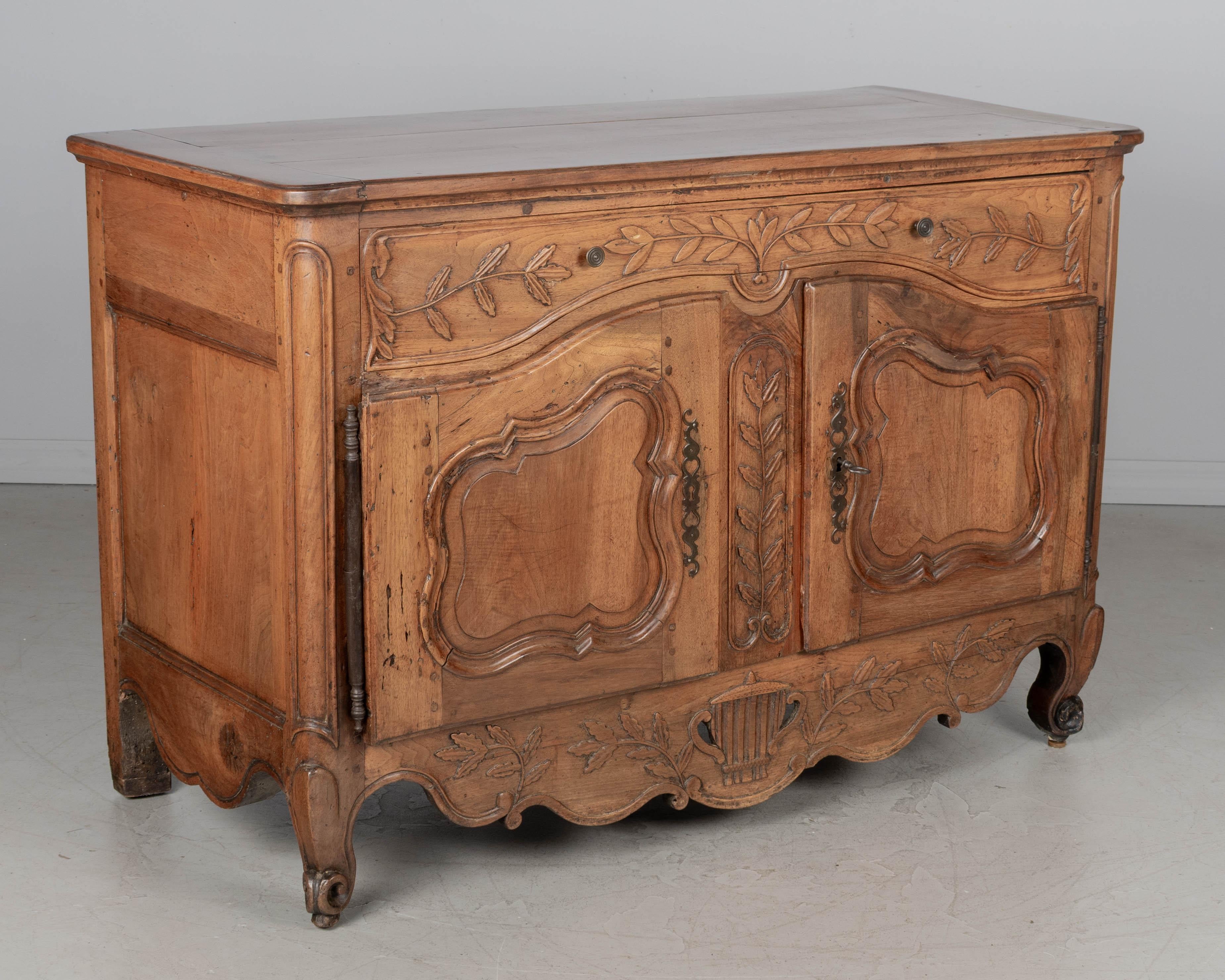 An 18th century French Louis XV Provençal buffet made of solid walnut with pierced carved apron below two curved doors. Nicely detailed with carvings of leafy branches and a center urn on the scalloped apron. Original iron hardware on the doors with