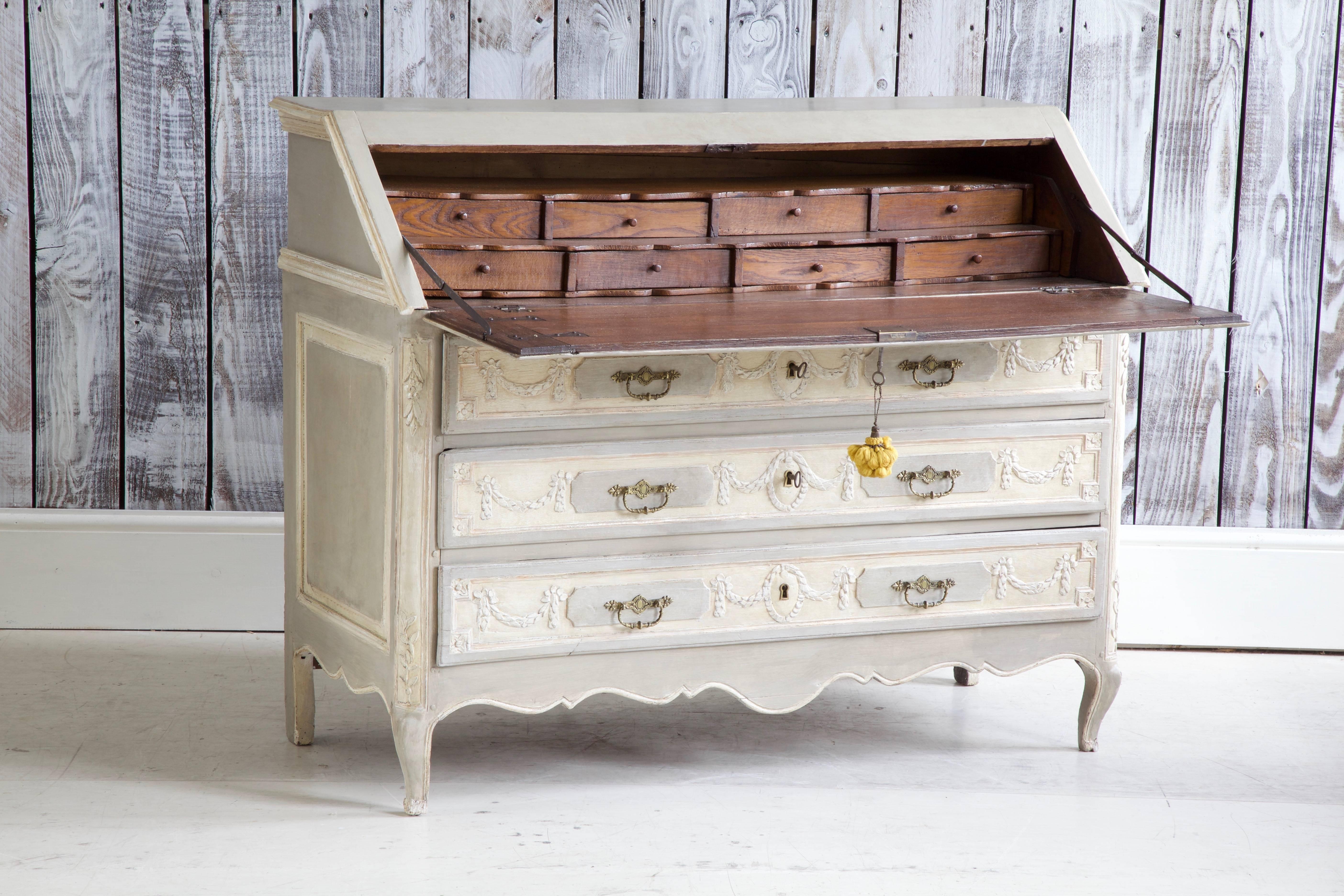 18th century, French, Louis XVI writing desk/scriban decorated with hand carved, swathes of laurel leaf across the top section and drawers, painted in two tones of French grey with warm white highlights, moderately aged and distressed. The drop leaf