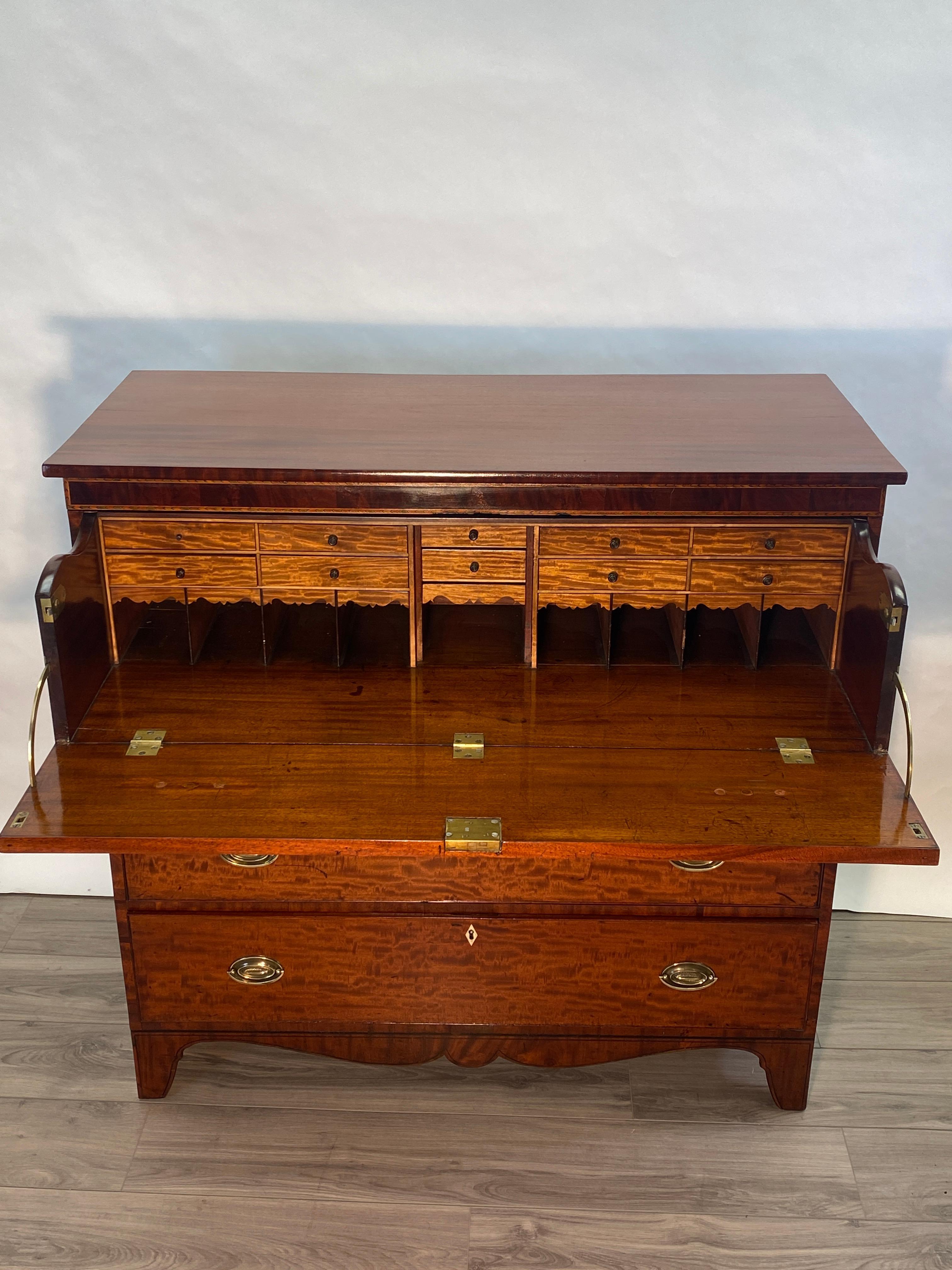 A highly figured mahogany American Federal period butlers chest with three lower drawers. The upper fall front drawer opens to reveal three additional drawers and pigeon holes. Brass pulls, Resting atop shaped bracket feet. 

America, Circa