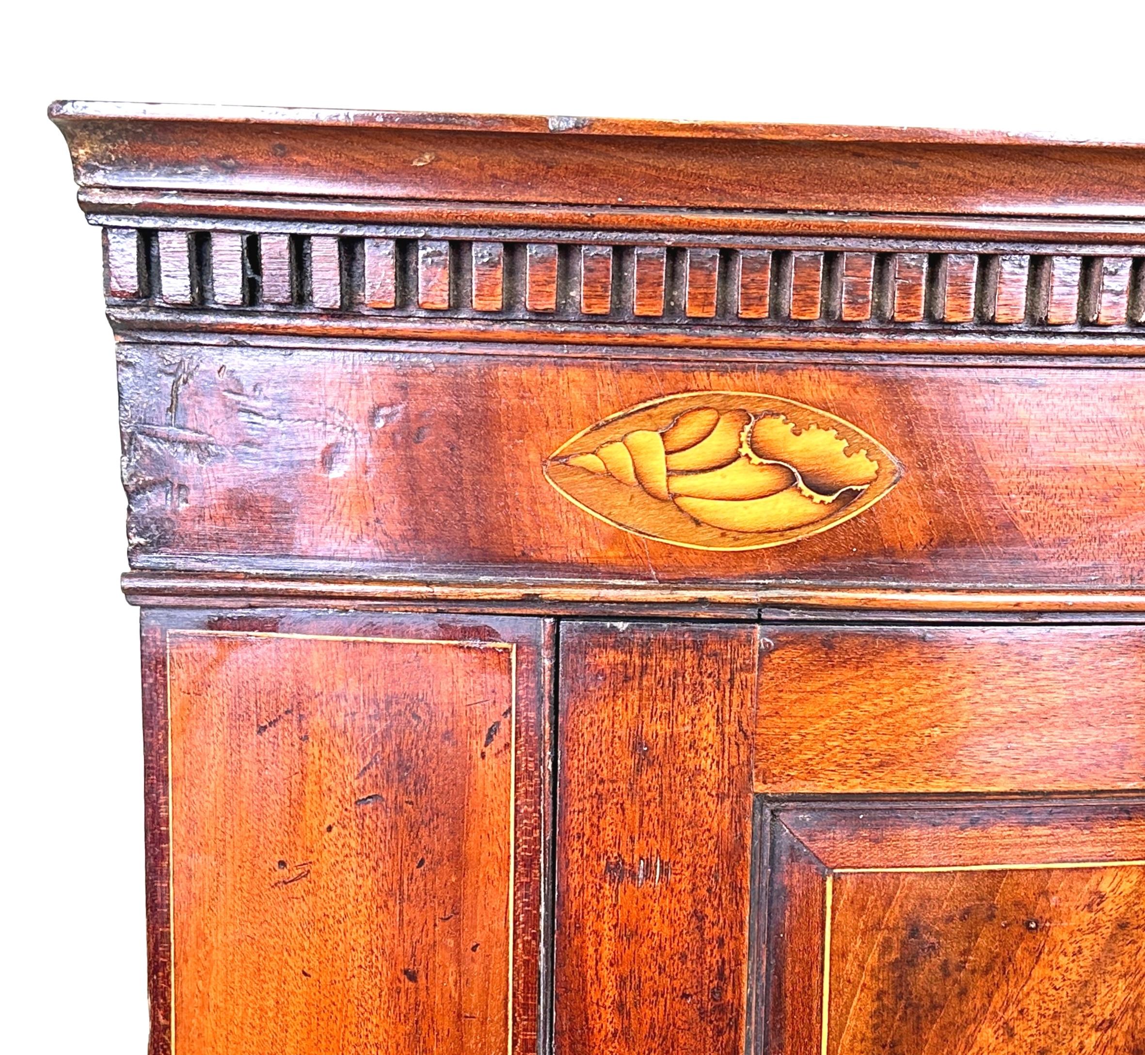 Credenza angolare pensile in mogano con fronte ad arco, della fine del XVIII secolo, di ottima qualità, con un'attraente decorazione a intarsio di conchiglie sul cornicione, sopra una coppia di ante a pannelli di ottima fattura, che racchiudono tre
