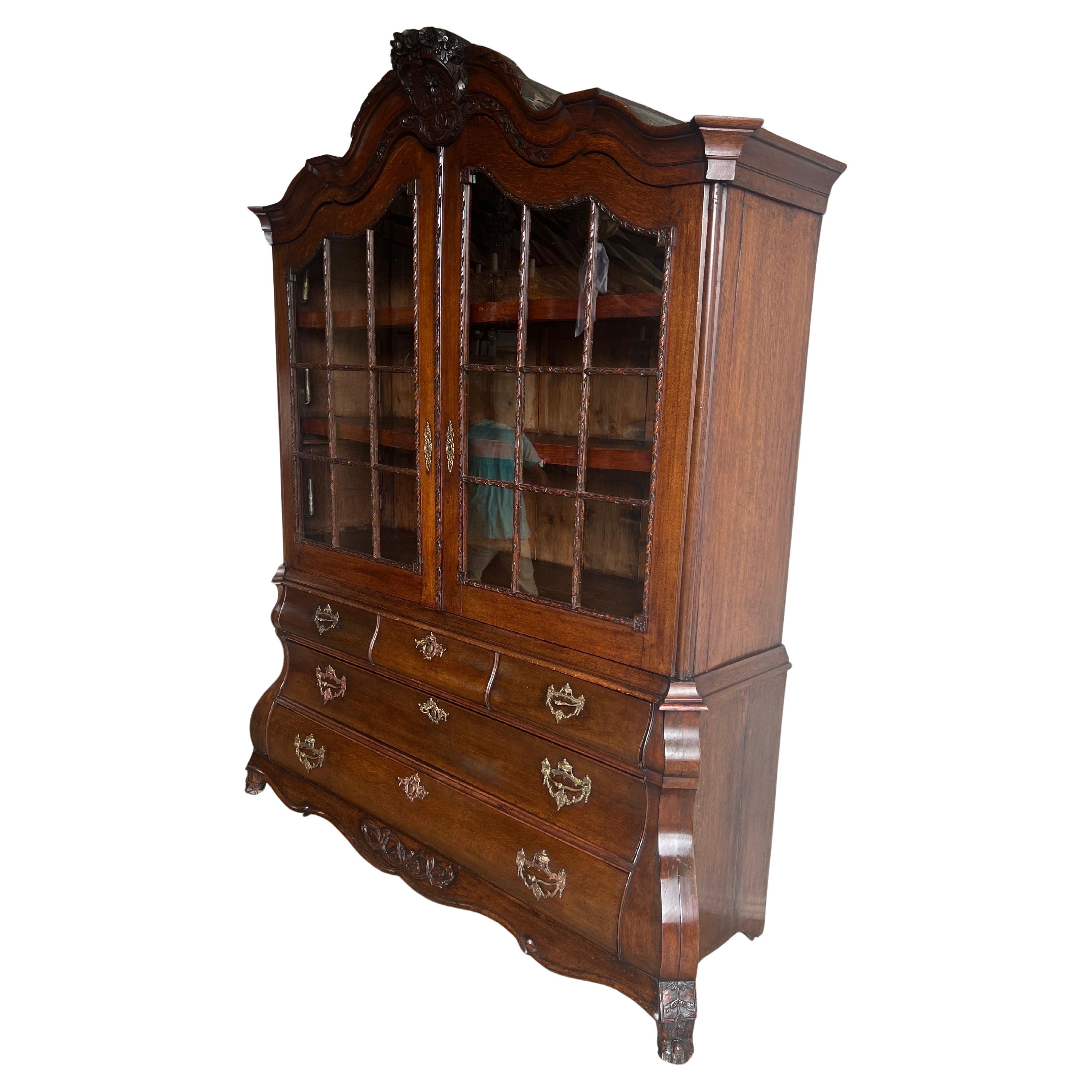 An exceptional 18th-century Dutch display cabinet, richly carved and beautifully proportioned, featuring a dramatic bombe base and finely glazed serpentine doors. Crafted from solid walnut with a deep, lustrous patina, this piece showcases the