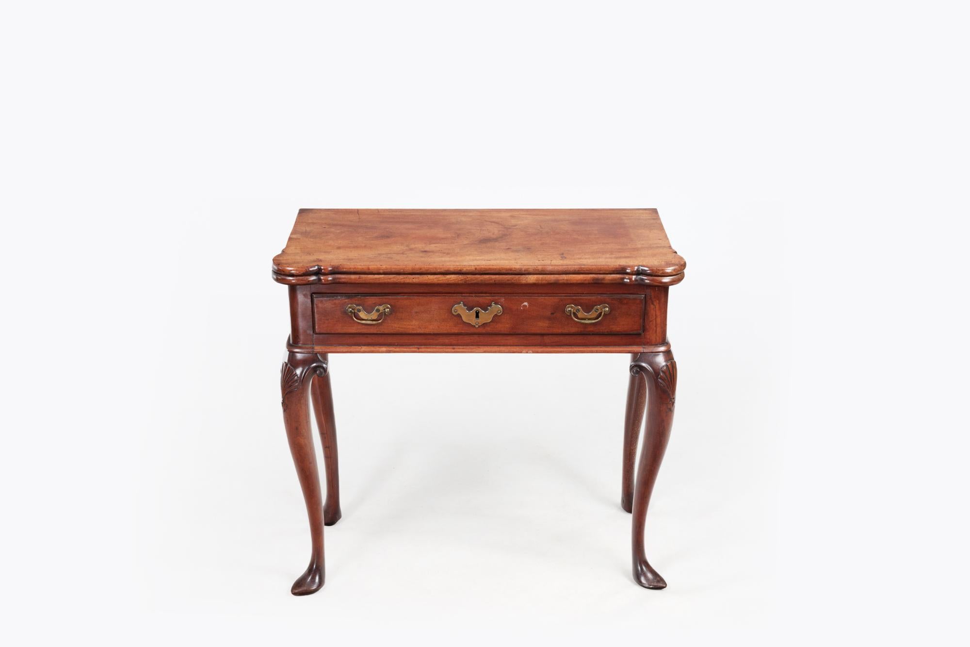 18th Century mahogany fold-over tea table with shaped top. Unusual for this type of piece, it sits on four matching cabriole legs with scallop and scroll decoration to the knees and terminates on slipper feet. The single drawer to the front is