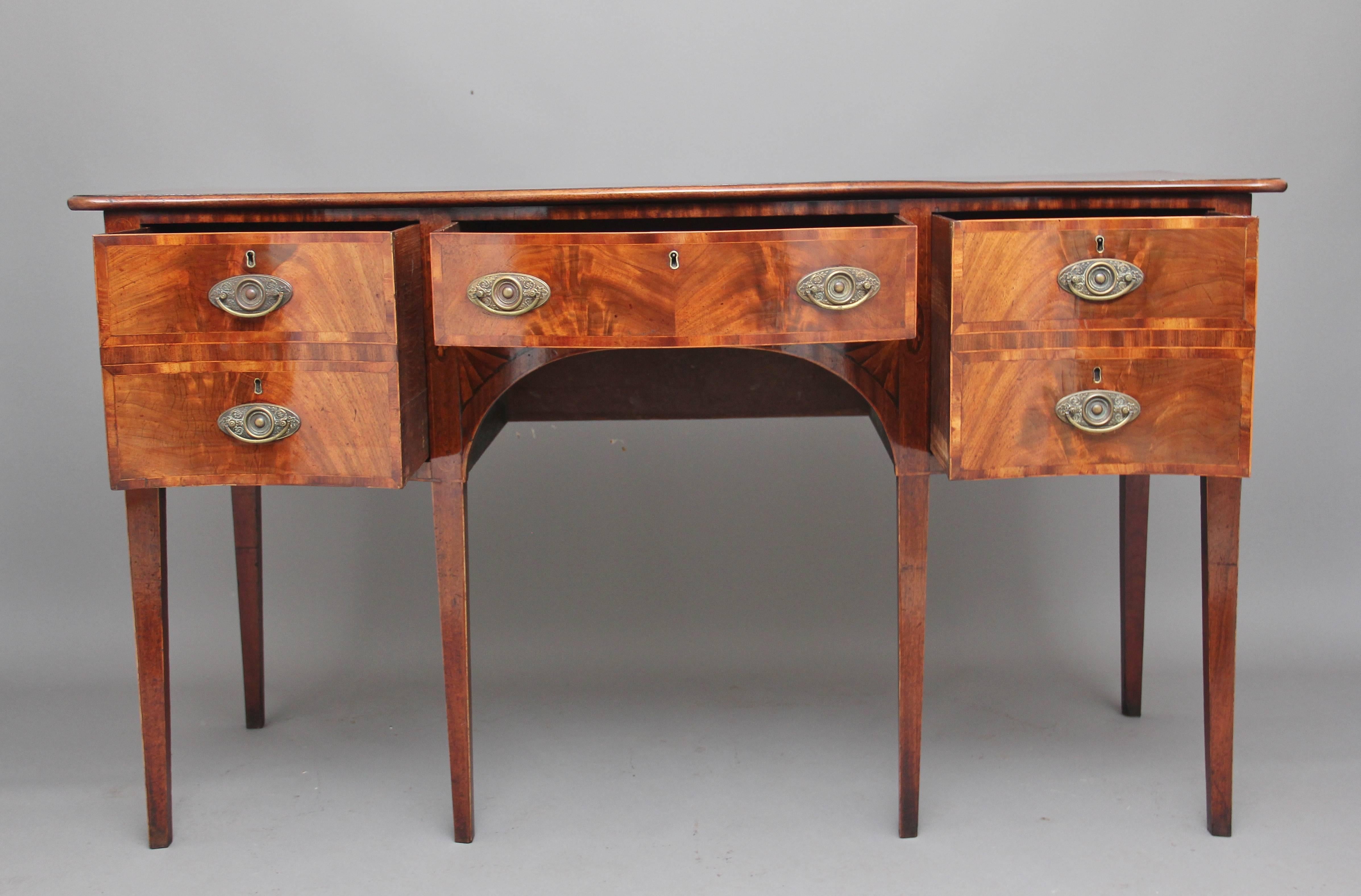 18th century mahogany inlaid serpentine sideboard, the shaped top crossbanded and having a moulded edge, with three oak lined drawers below with oval brass plate handles, the drawer fronts also crossbanded, the front of the sideboard having boxwood