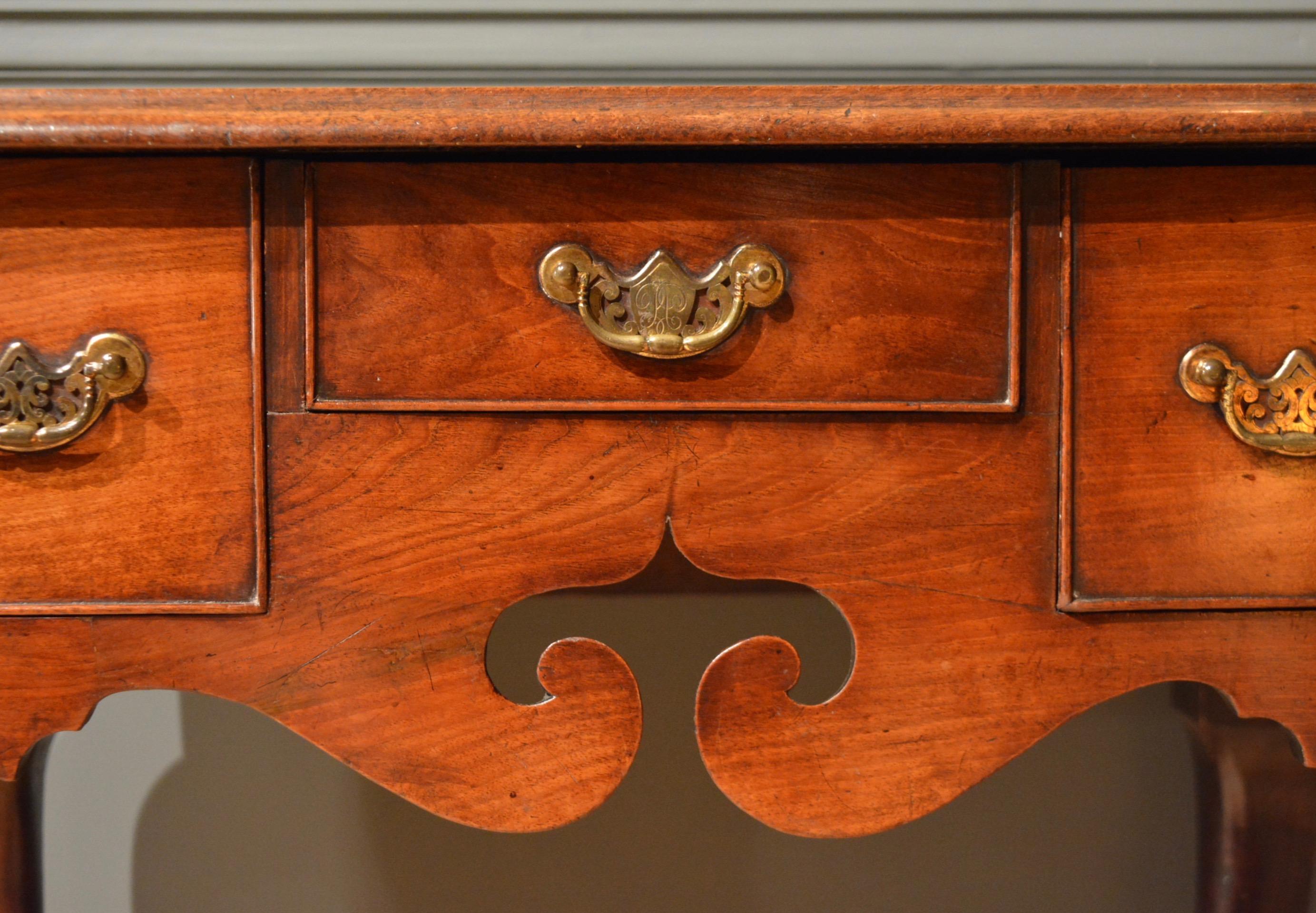 A George II mahogany lowboy standing on finely shaped cabriole legs finished with faceted pad feet (often thought to indicate an Irish origin) the three drawers retaining their original engraved handles, the central one containing a cipher.