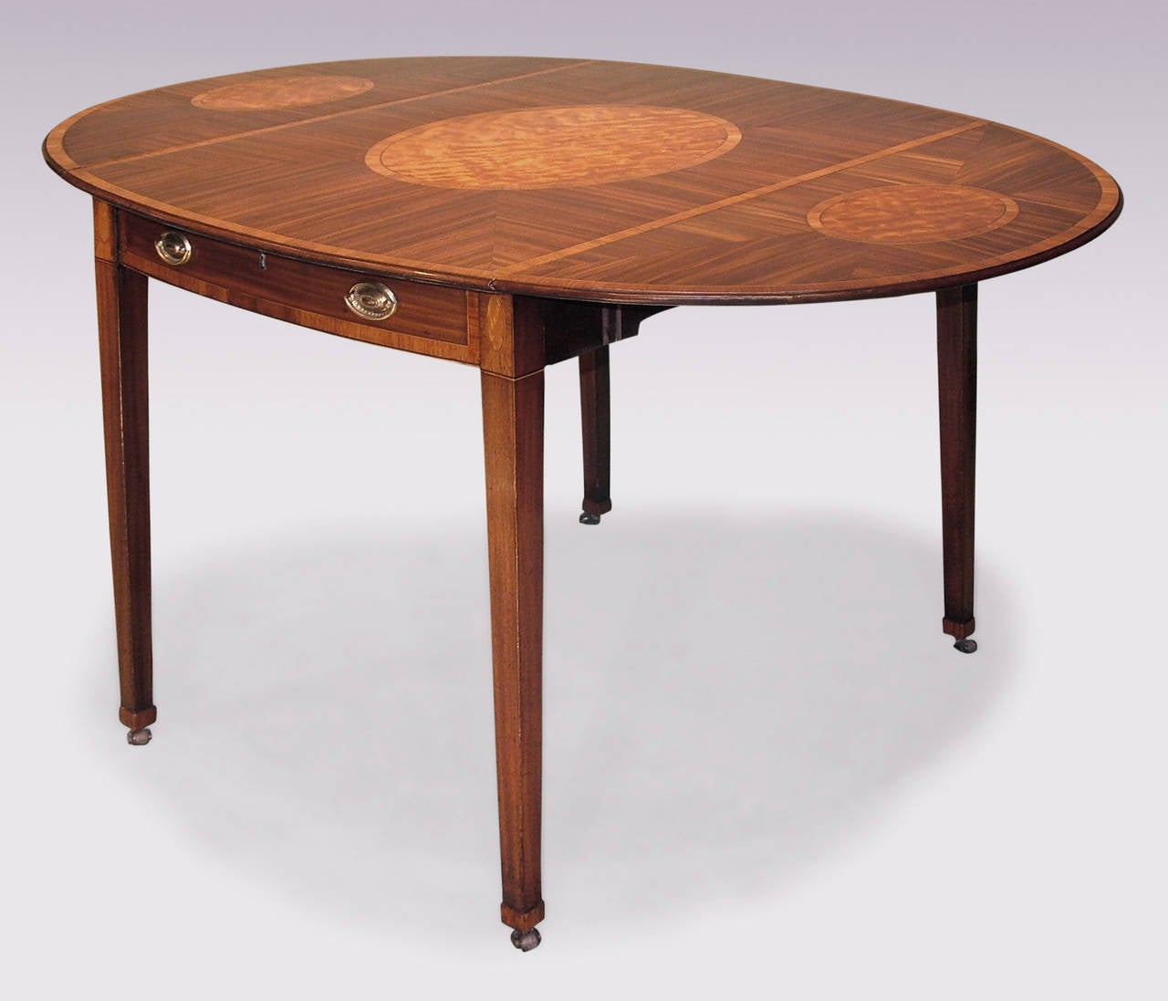 A large late 18th century Sheraton period mahogany Pembroke table having tulipwood cross banded mitred oval top, centred by oval satinwood panels to centre and flaps, above dummy frieze drawers supported on square tapering legs ending on collars and