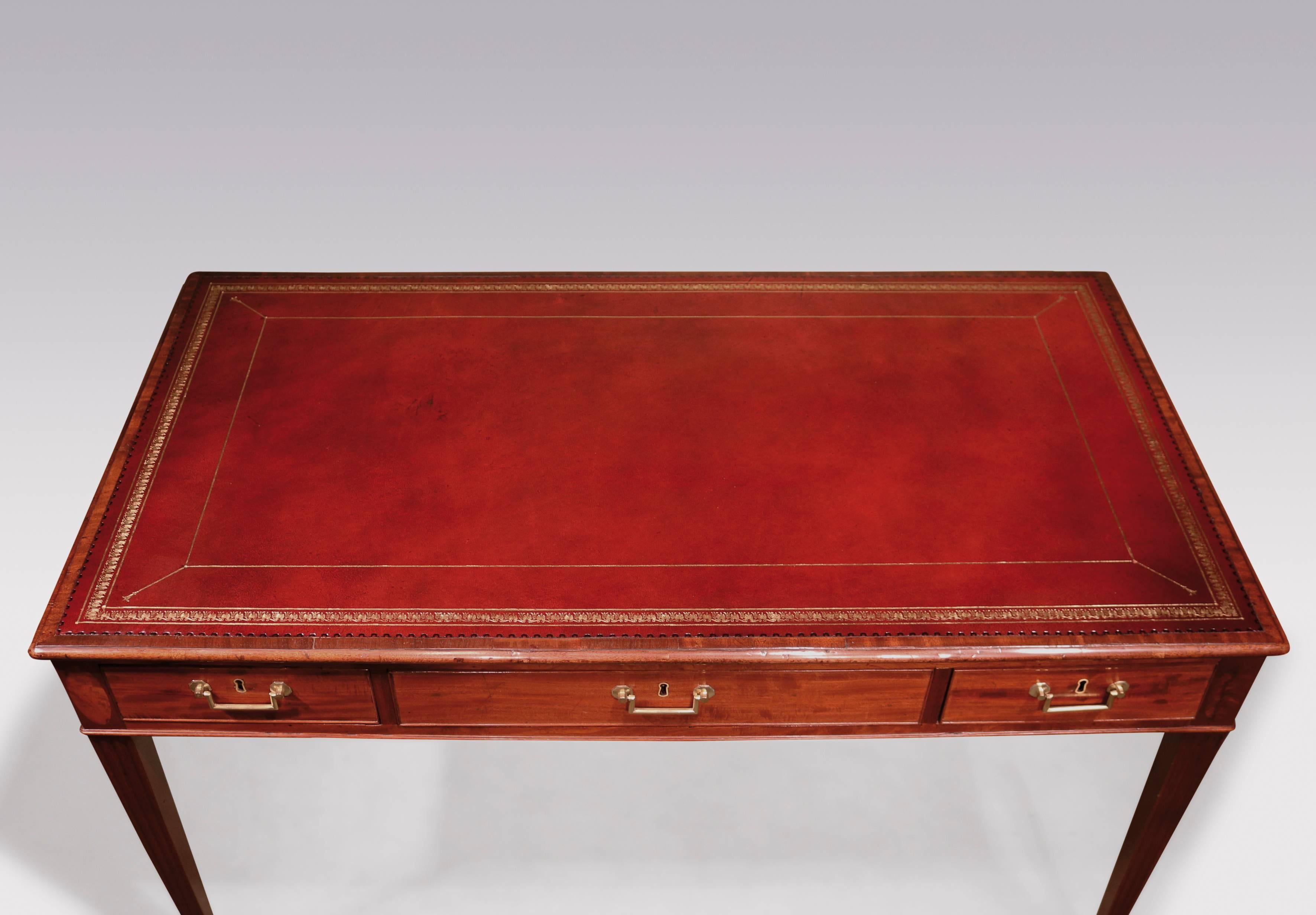 A late 18th century George III period well figured mahogany writing table, having a moulded edged red gilt tooled leather top, above six cockbeaded drawers retaining original handles, supported on fluted square tapering legs with veneered oval