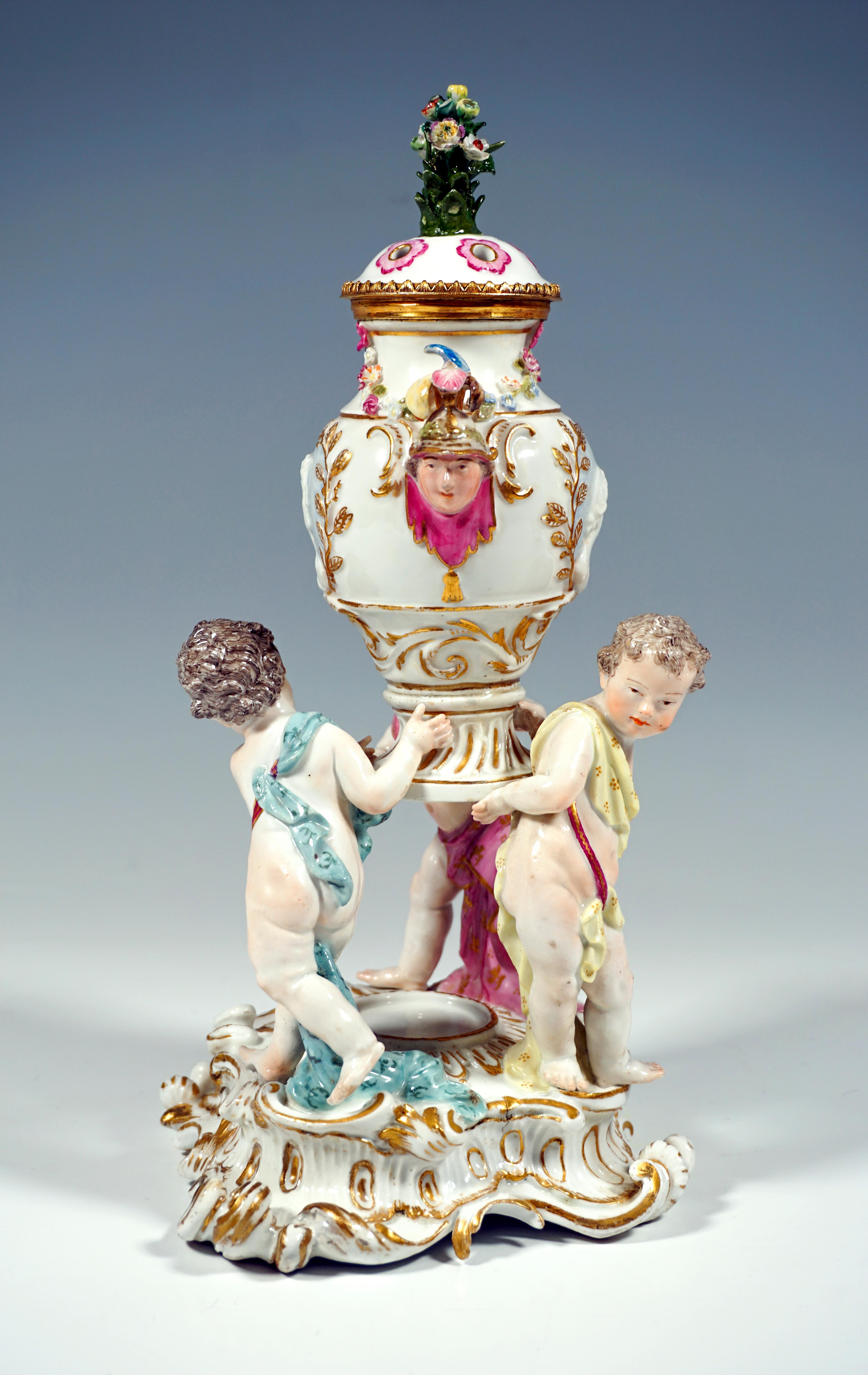 Very early and rare Meissen Group:
Three cupids, clad only with cloths tied together by ribbons, carrying a richly decorated fragrance vessel: the front and back of the baluster-shaped container is adorned with relief busts framed by gilded laurel
