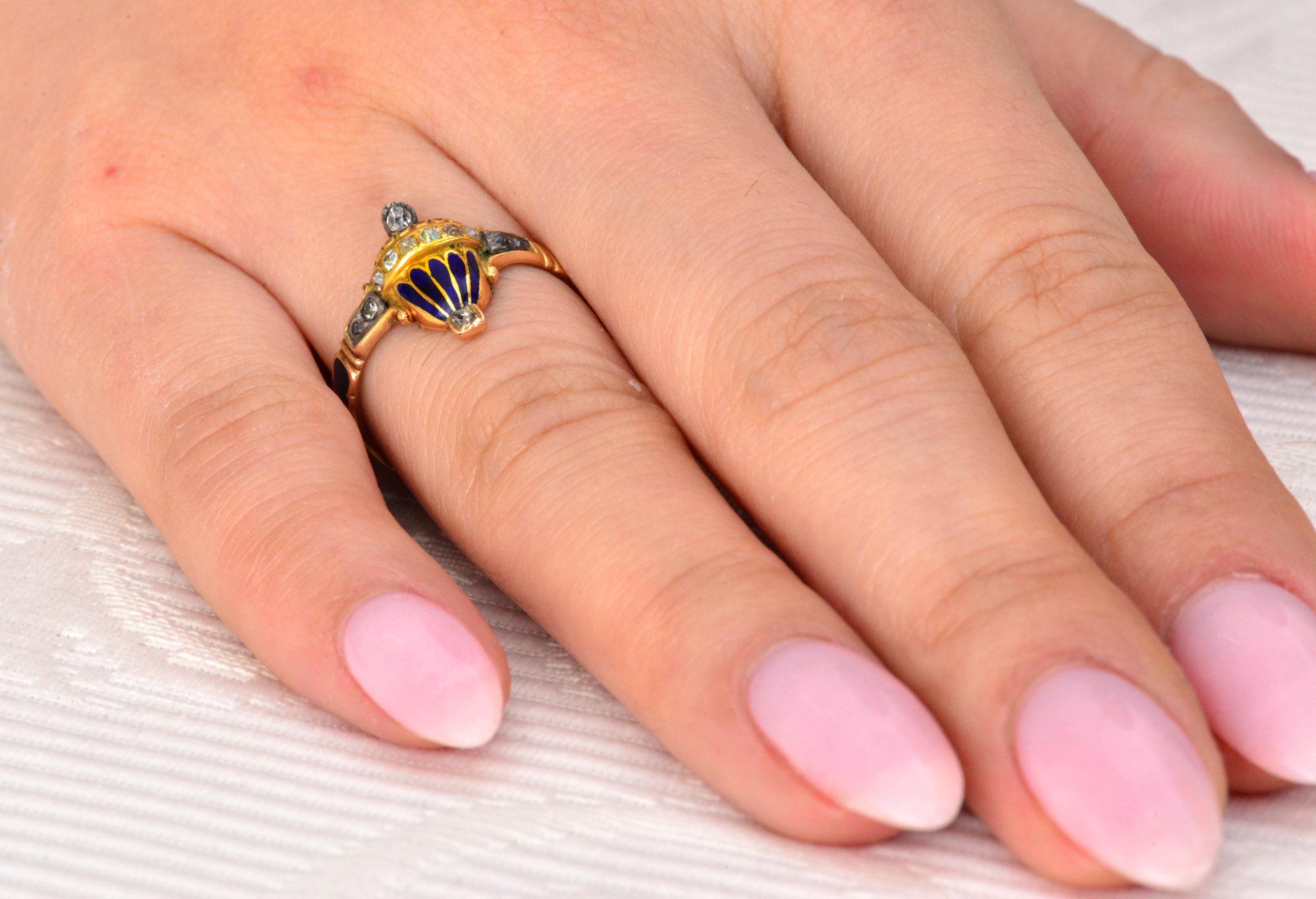 An 18th Century Memorial ring in the form of a blue enamel urn set at the front and shoulders with rose cut diamonds and set with a single rose cut diamond on the opposing terminals of the ring. The back of the ring contains a hinged compartment for