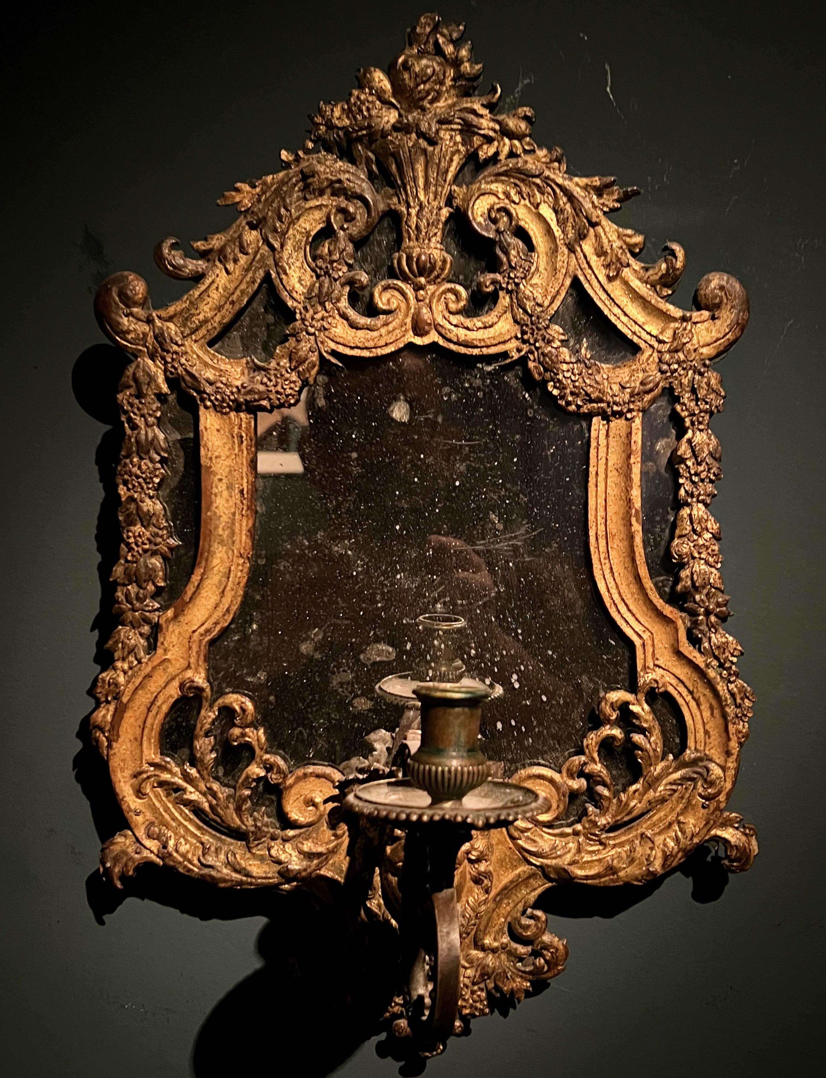 A very charming early 18th century mirror with framework of gilt lead and a bronze candle arm. The cast gilt lead decoration is mounted on a wood base. This mirrored wall sconce is possibly Swedish from the Precht workshops and from the late baroque