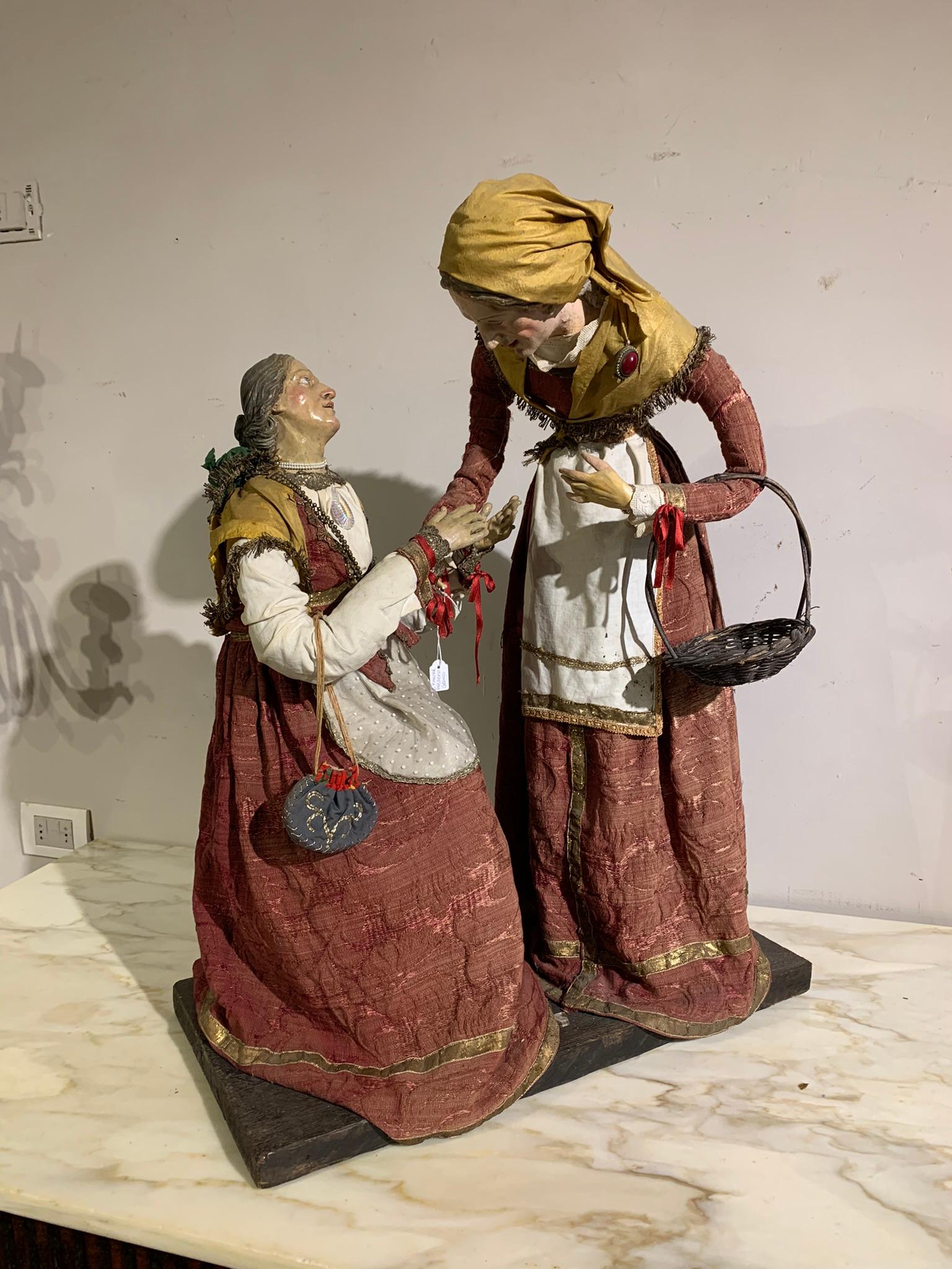 Beautiful pair of large church crib sculptures in wood and painted terracotta with glass eyes depicting a peasant girl helping a beggar woman, typical Neapolitan manufacture from the mid-18th century embellished with small collectible jewels.