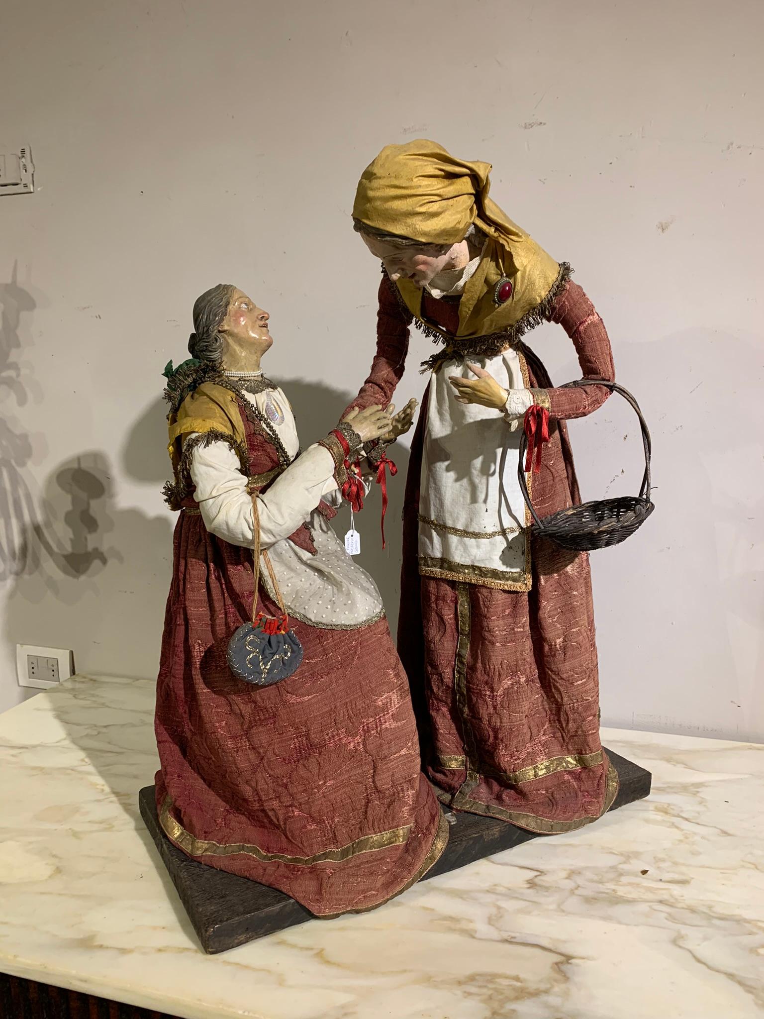 Bellissima coppia di grandi sculture da presepe in legno e terracotta dipinta con occhi in vetro raffiguranti una contadina che aiuta una mendicante, tipica manifattura napoletana della metà del XVIII secolo impreziosita da piccoli gioielli da